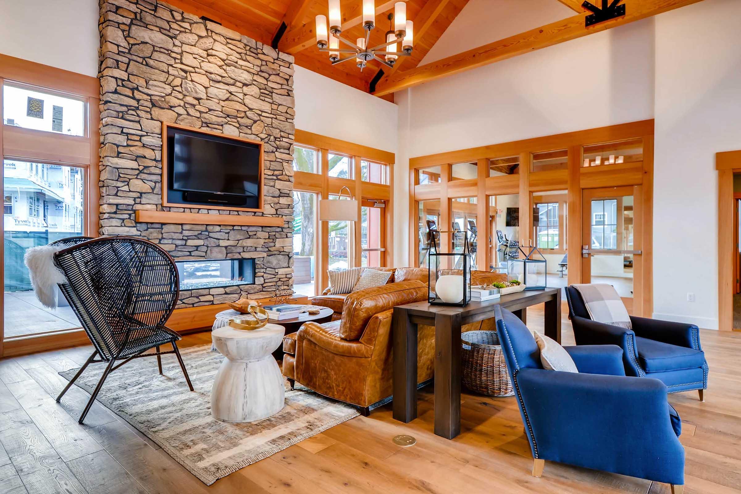 A cozy living room featuring a stone fireplace with a mounted TV, large windows, and wooden beams.