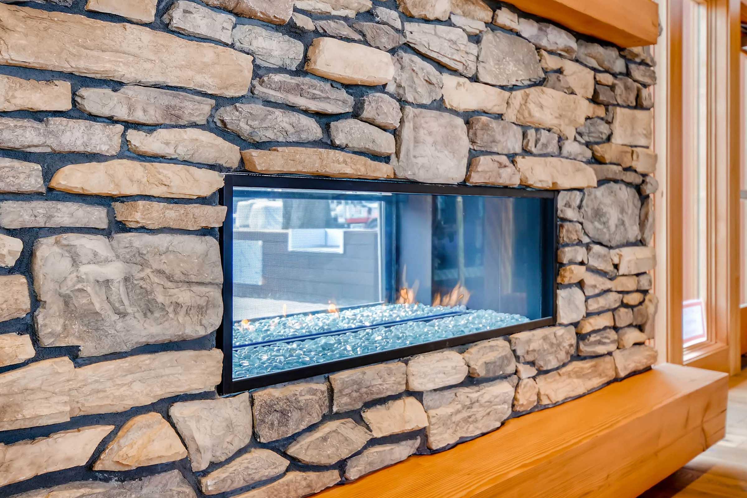 A modern stone fireplace featuring a sleek glass front, set against a rustic stone wall.