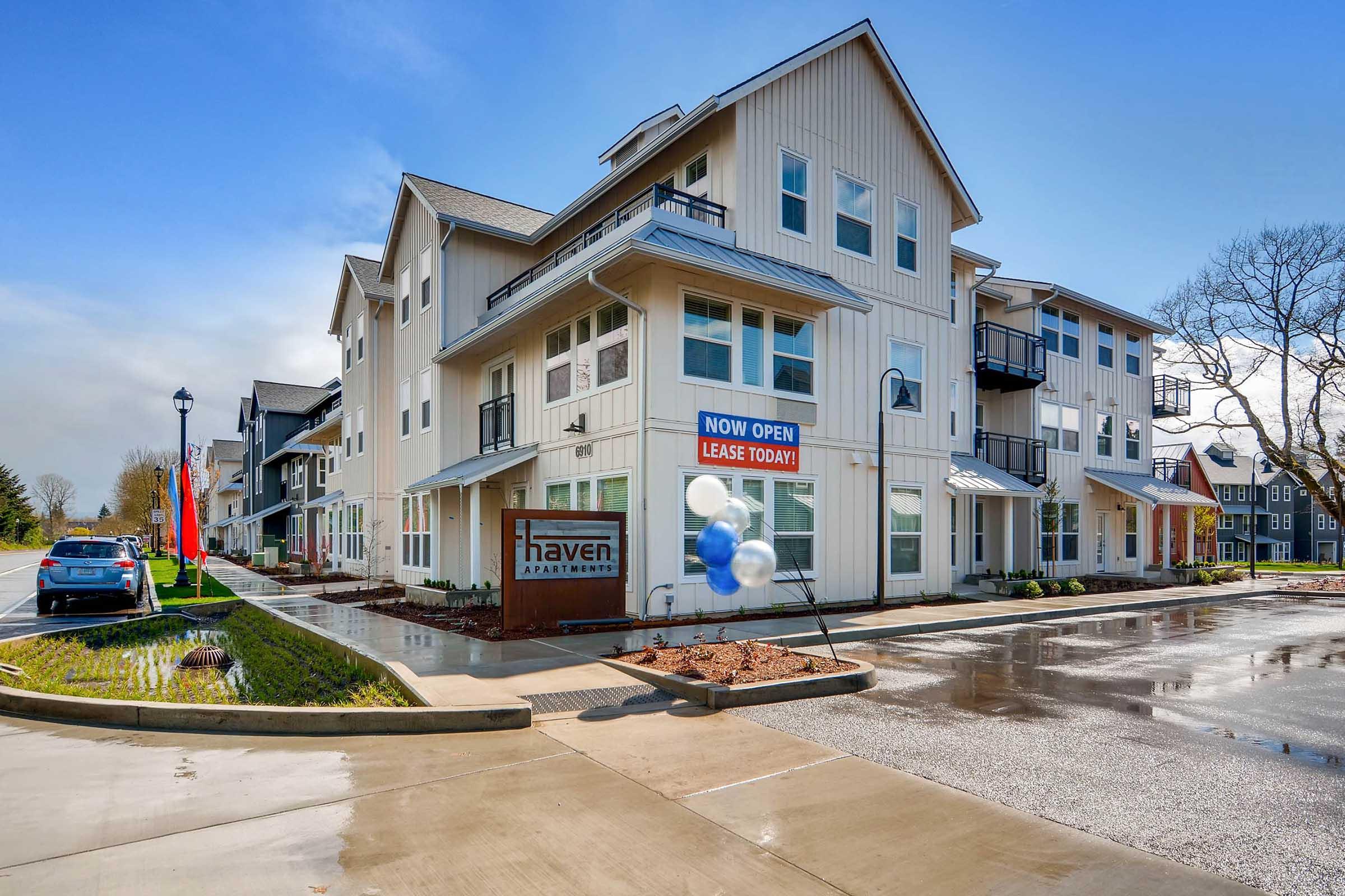 Newly opened Haven Apartments featuring a modern multi-story building with large windows, a welcoming sign, and balloon decorations.