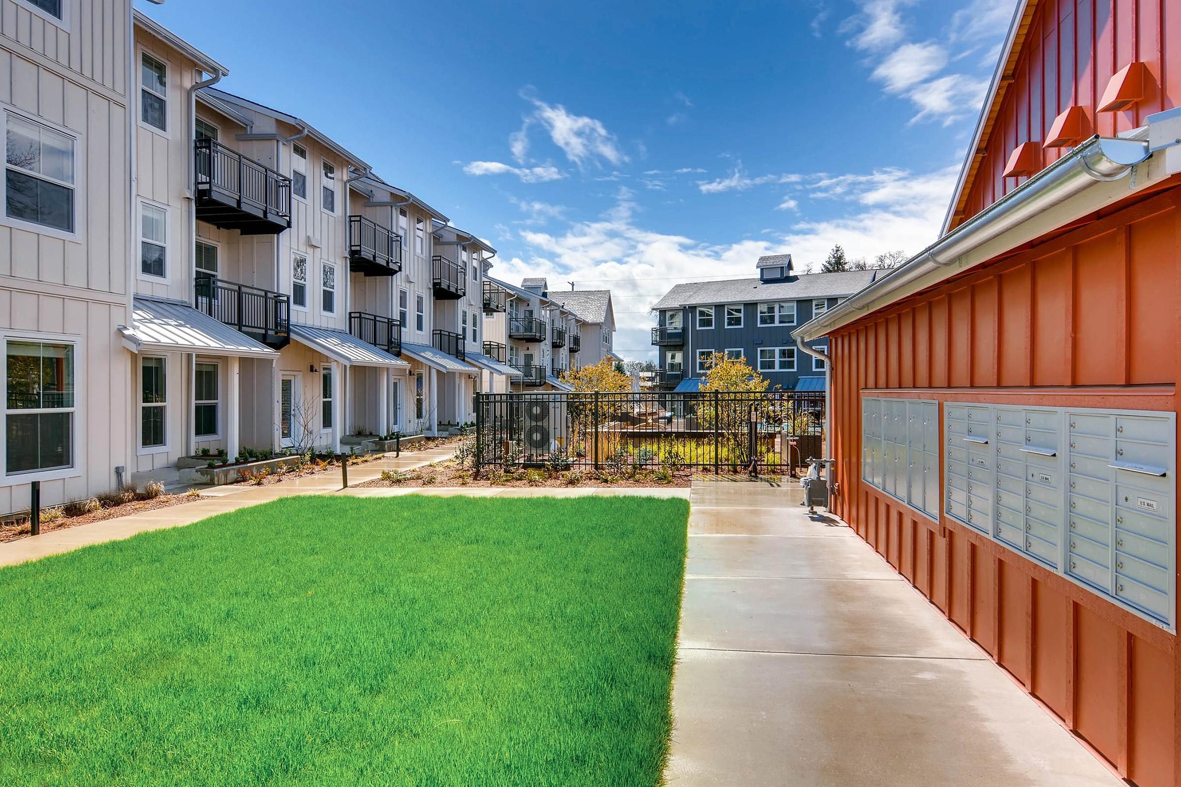 A landscaped courtyard featuring well-maintained green grass and paving, surrounded by modern residential buildings with balconies.