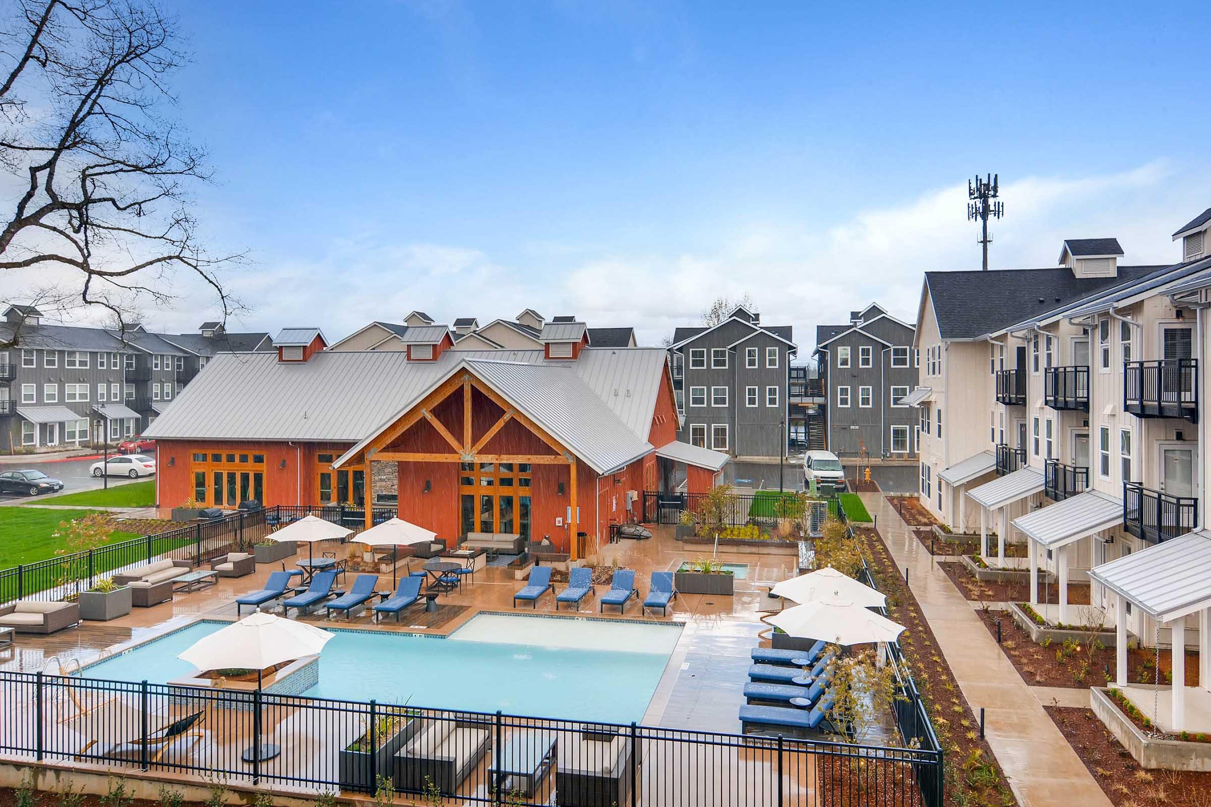 A modern residential complex featuring a swimming pool surrounded by lounge chairs and umbrellas.