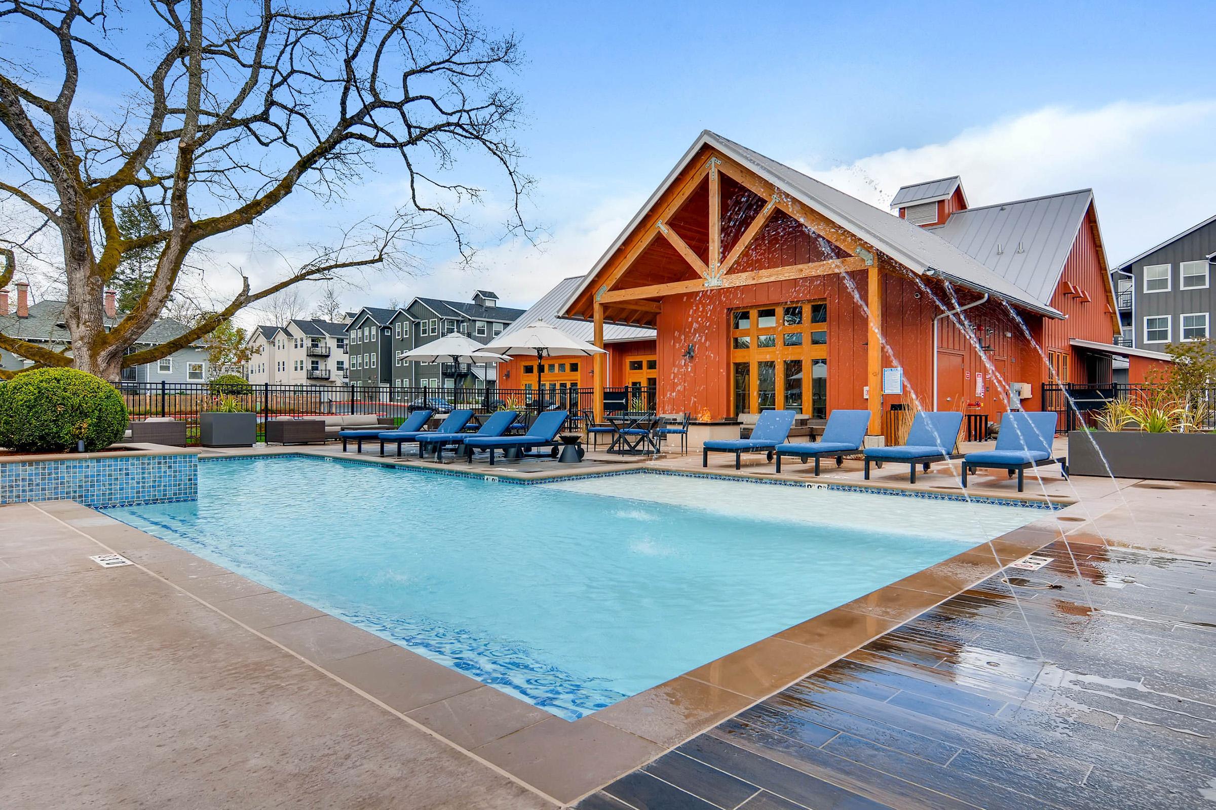 A tranquil outdoor pool area with blue lounge chairs and a modern building featuring a wooden A-frame design in the background.