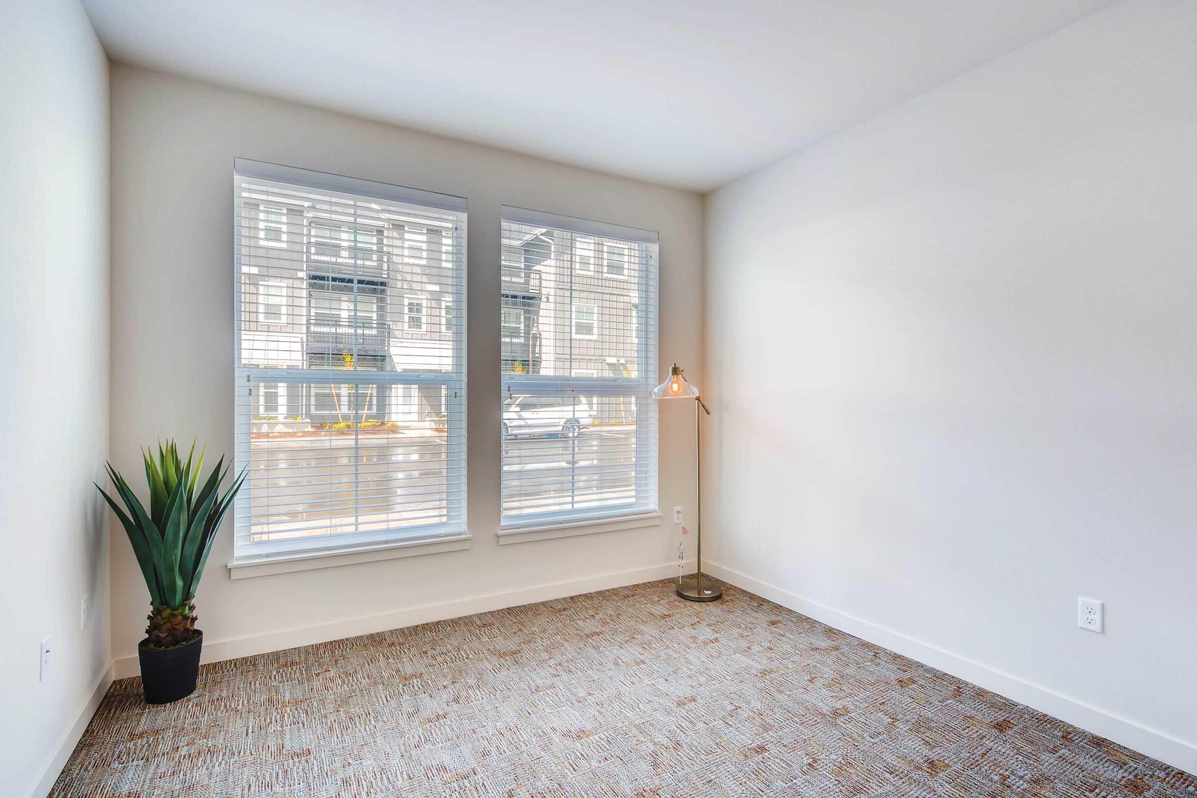 A bright, empty room featuring two large windows with blinds, allowing natural light to enter.