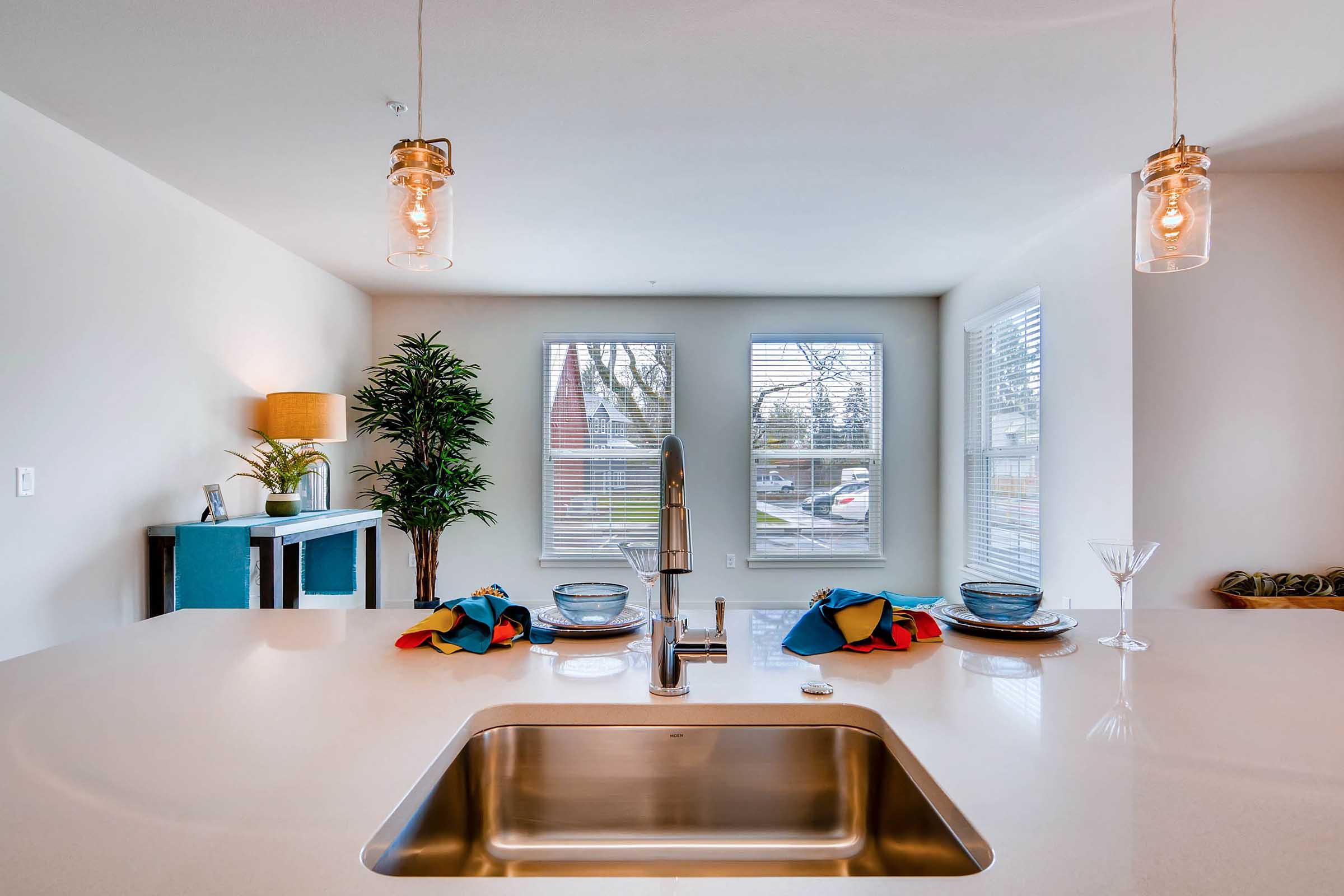 A modern kitchen featuring a sleek countertop with a stainless steel sink, decorative plates, and colorful napkins.