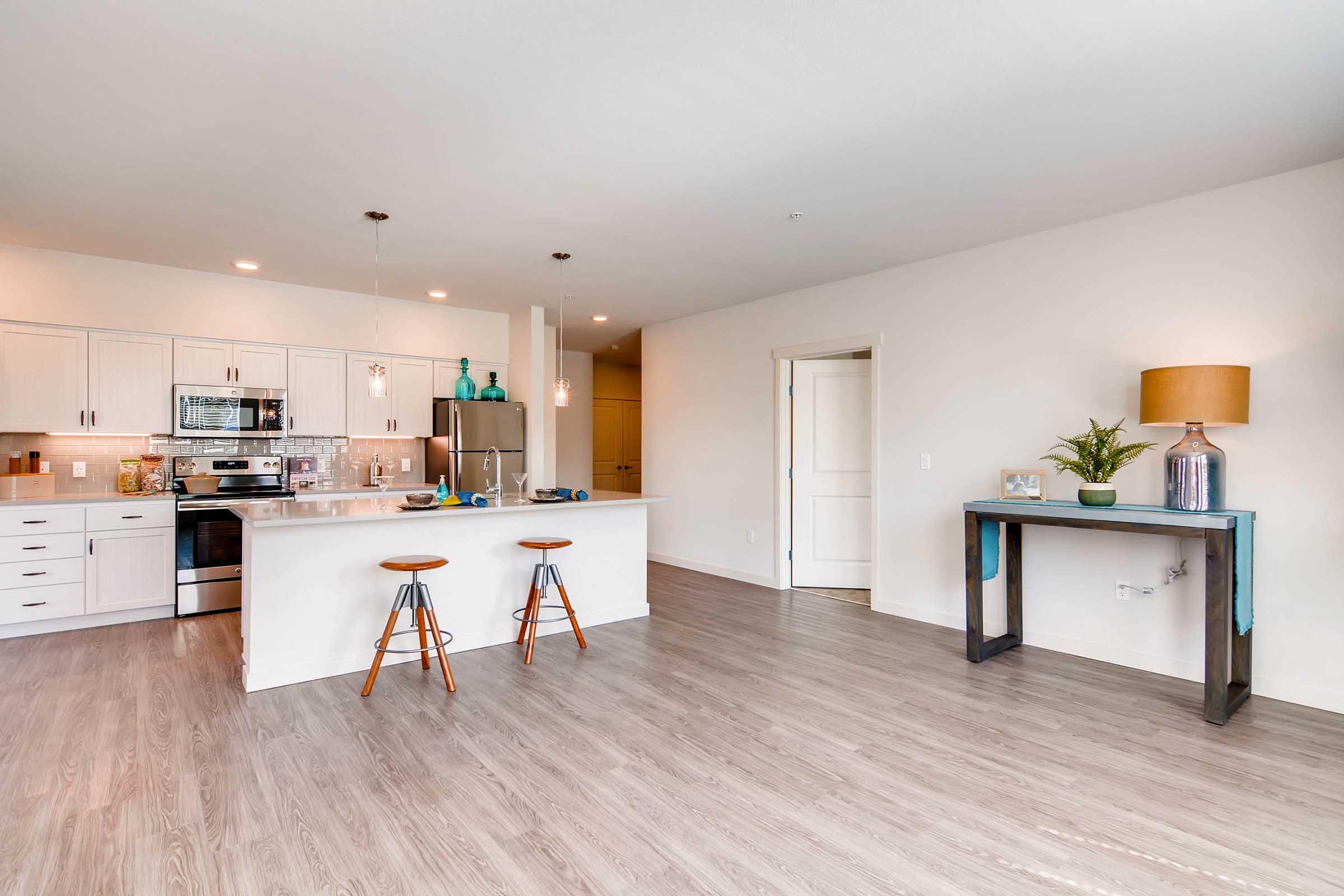 A modern kitchen and living area featuring a white cabinetry kitchen with stainless steel appliances, a central island with seating, and a stylish dining area.
