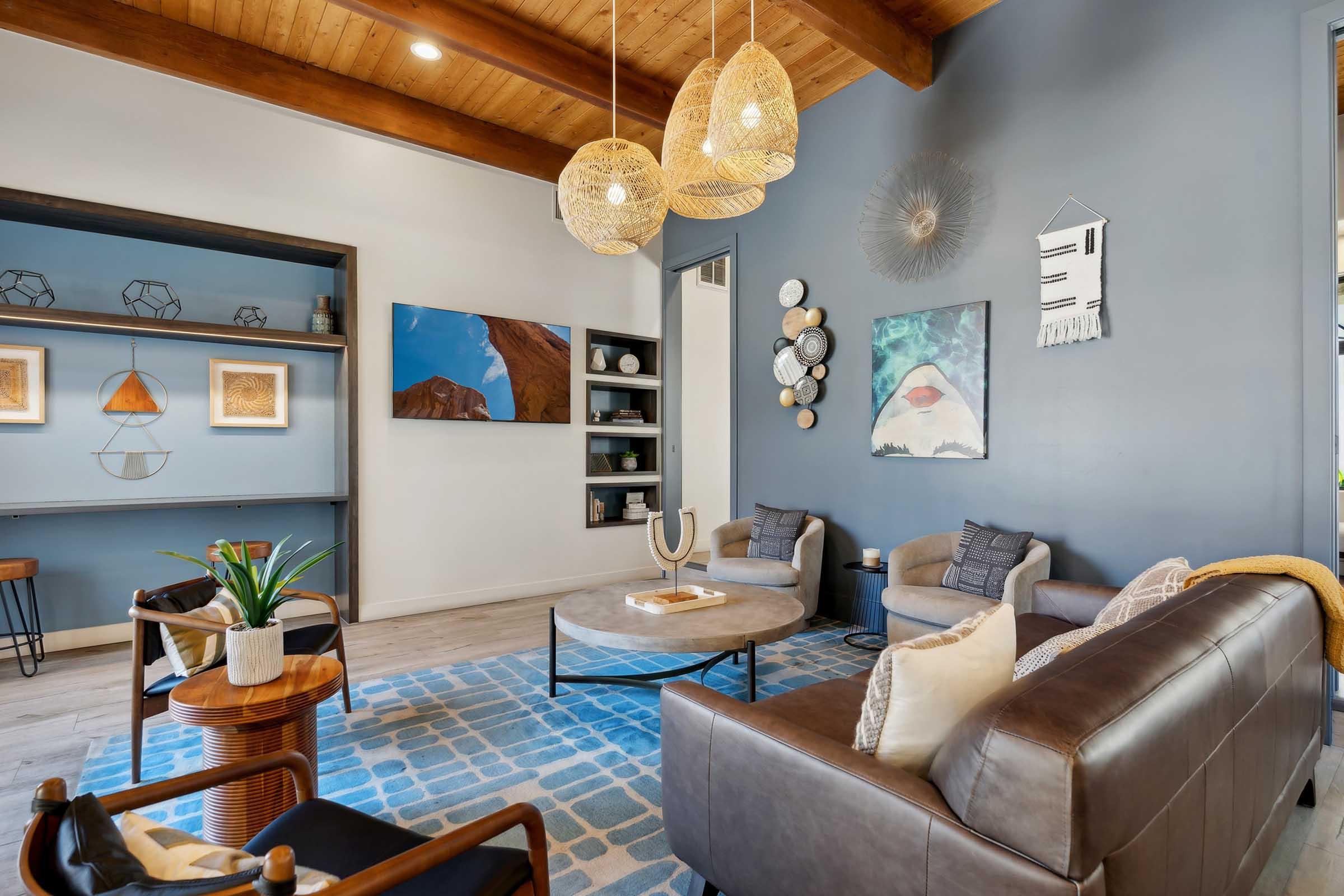 A stylish living room featuring a modern design with a round coffee table, comfortable seating, and decorative wall art. The space includes a blue rug, wooden beams on the ceiling, and natural light enhancing the cozy atmosphere. Elegant light fixtures and decorative accents add to the contemporary aesthetic.