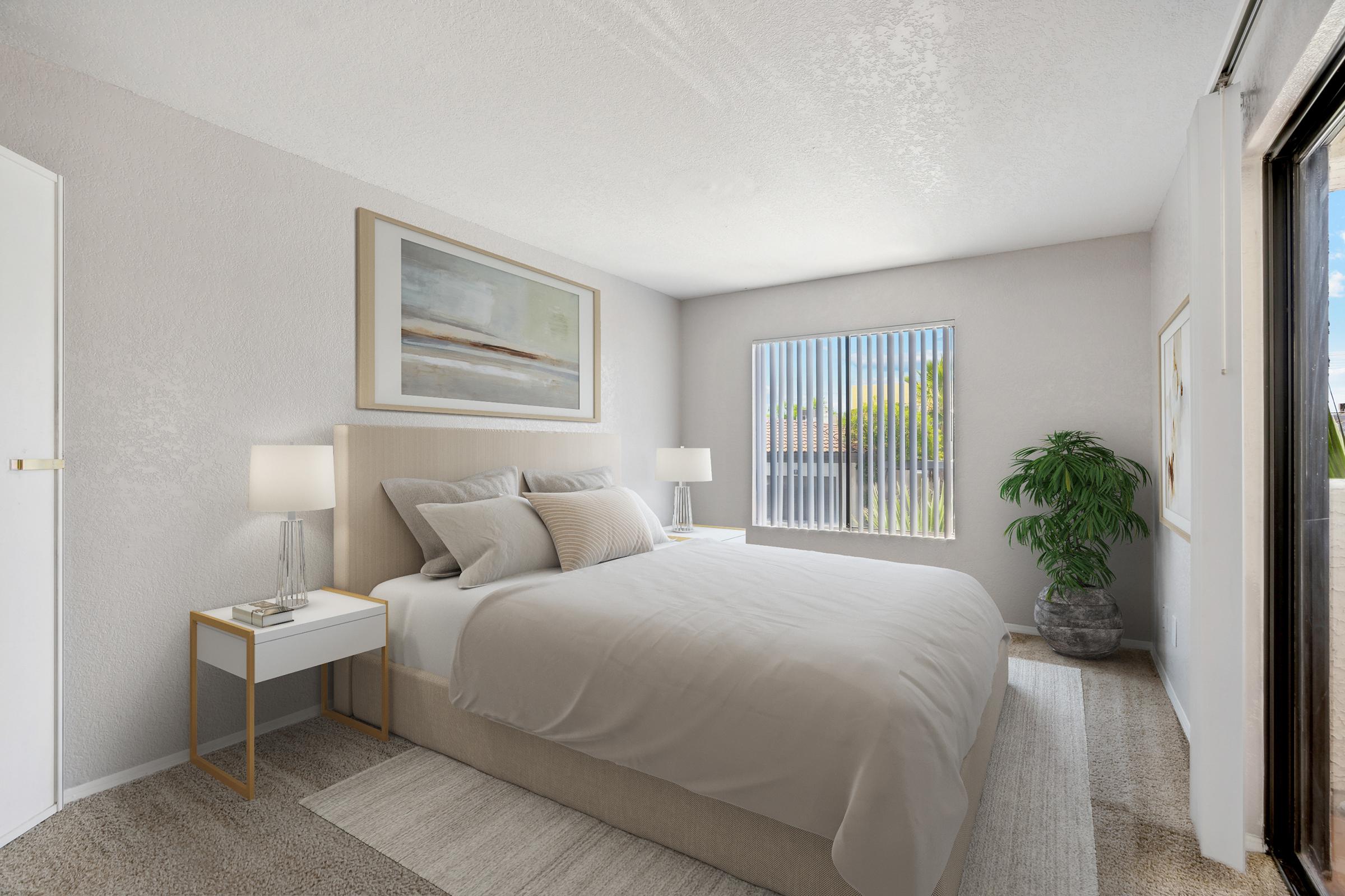 A cozy bedroom with a light-colored theme. It features a bed with neutral linens, bedside tables with lamps, and a large window with vertical blinds. A decorative plant adds a touch of greenery, and artwork is displayed on the wall, creating a bright and inviting atmosphere.