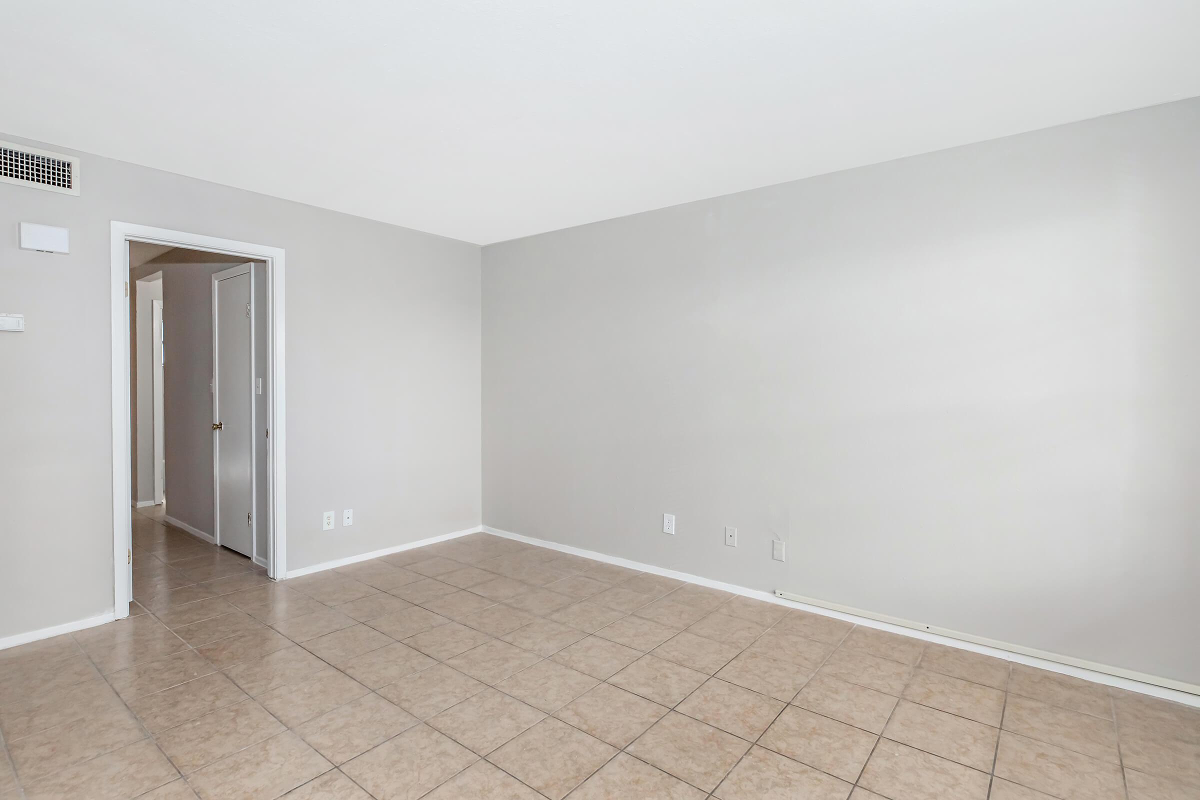 Empty room with smooth, light gray walls and a tiled floor. A doorway leads to another room, and there are no visible furnishings or decorations, creating a spacious and minimalist appearance.