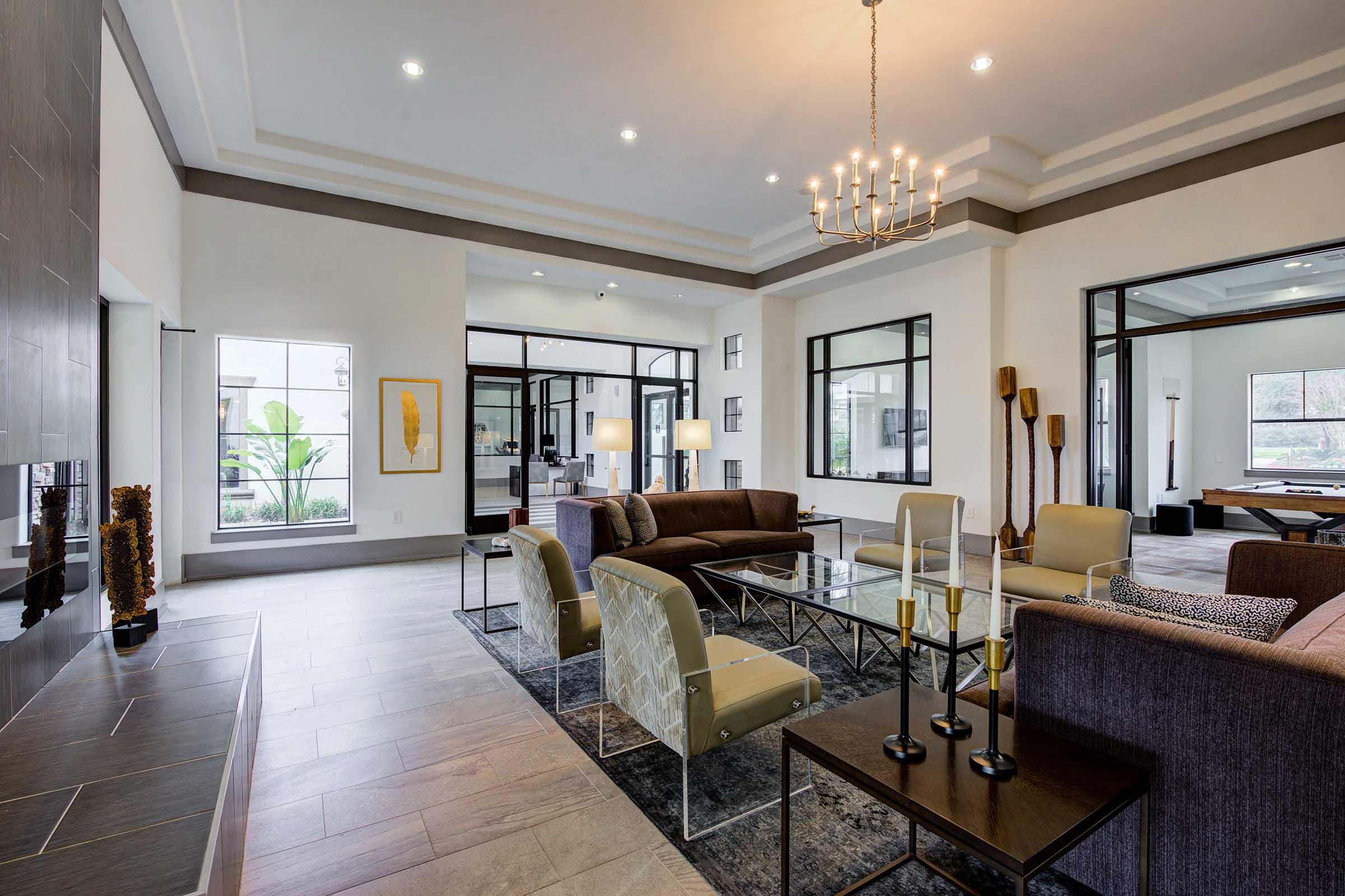 A modern living room featuring stylish furniture, including a sofa, armchairs, and a coffee table. Large windows allow natural light to fill the space, highlighting the neutral color palette and elegant decor. A chandelier hangs from the ceiling, adding a touch of sophistication.