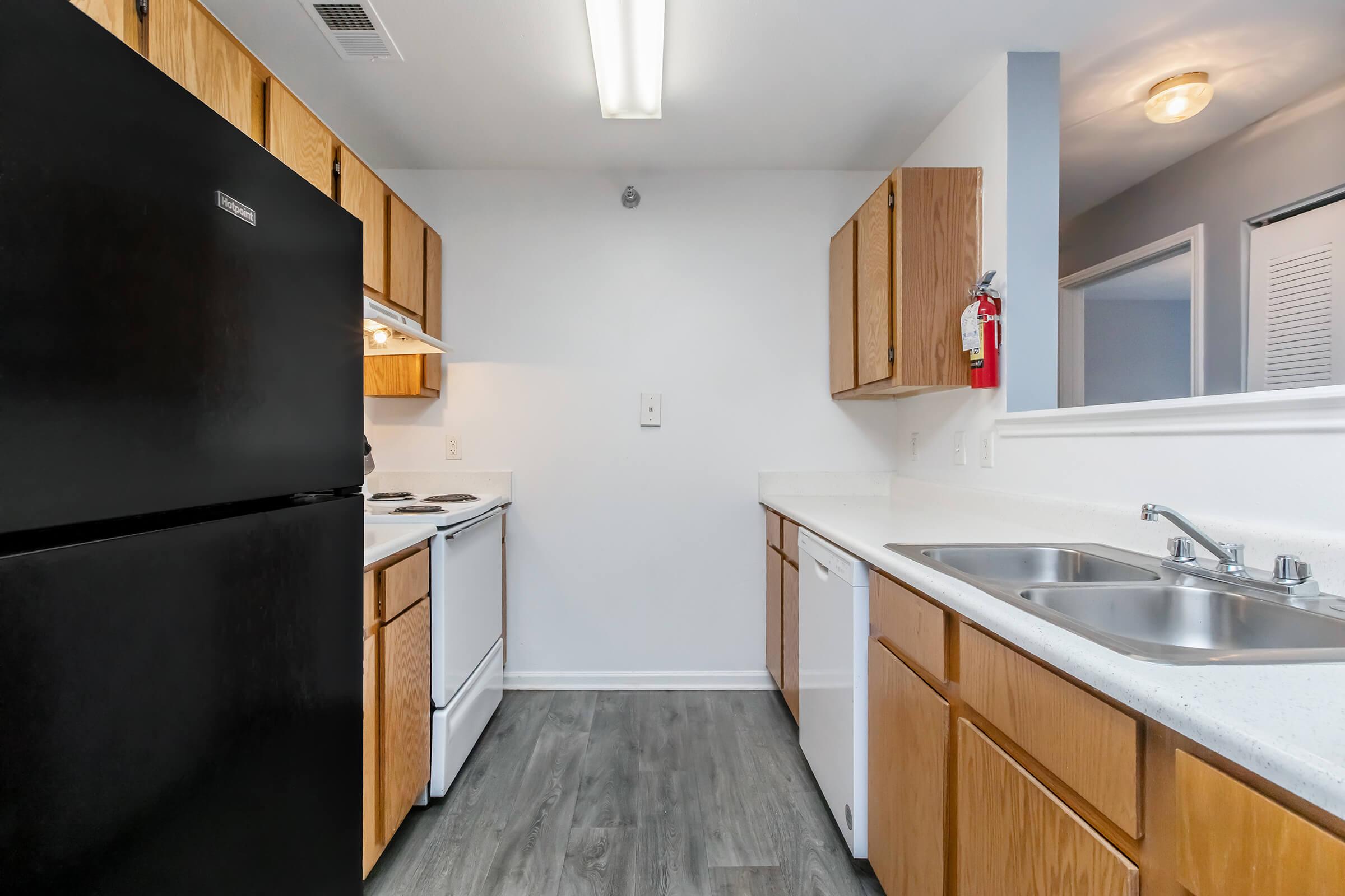Modern kitchen featuring dark cabinetry, white appliances, and a light-colored countertop. Includes a refrigerator, stove, dishwasher, and double sink. The space has a neutral color scheme with gray flooring and bright overhead lighting, providing a clean and inviting atmosphere.