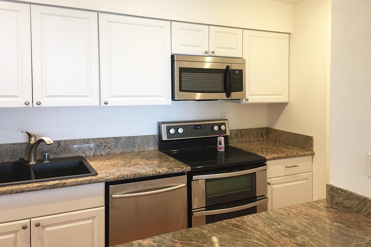 Modern kitchen featuring white cabinets, granite countertops with a beige and gray pattern, a stainless steel microwave, and an electric stove. Includes a black sink and a stainless steel dishwasher, creating a clean and contemporary look.