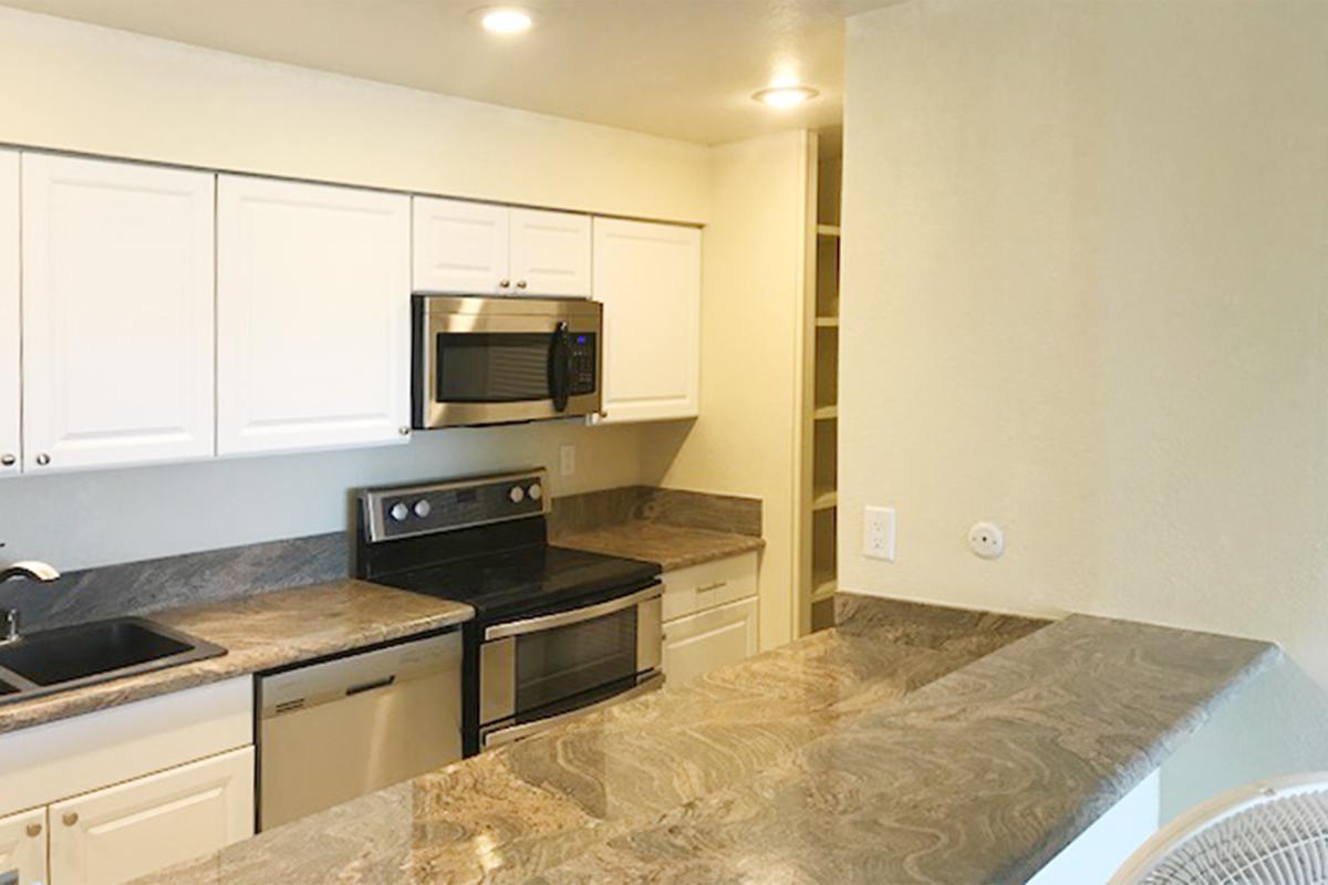 Modern kitchen featuring white cabinets, stainless steel appliances including a microwave and oven, a sleek countertop with a marble finish, and an adjacent pantry or storage space. Soft lighting enhances the ambiance, creating a clean and inviting cooking area.