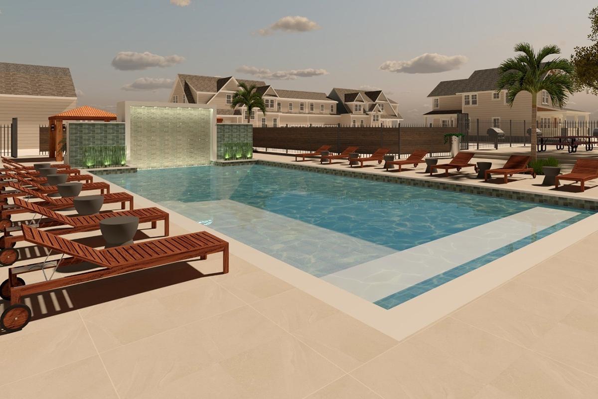 A serene outdoor pool area featuring a large swimming pool with a shallow ledge. Surrounding the pool are wooden lounge chairs with small tables. In the background, there are several residential buildings and palm trees. A waterfall feature adds ambiance to the space, enhancing the relaxed atmosphere.