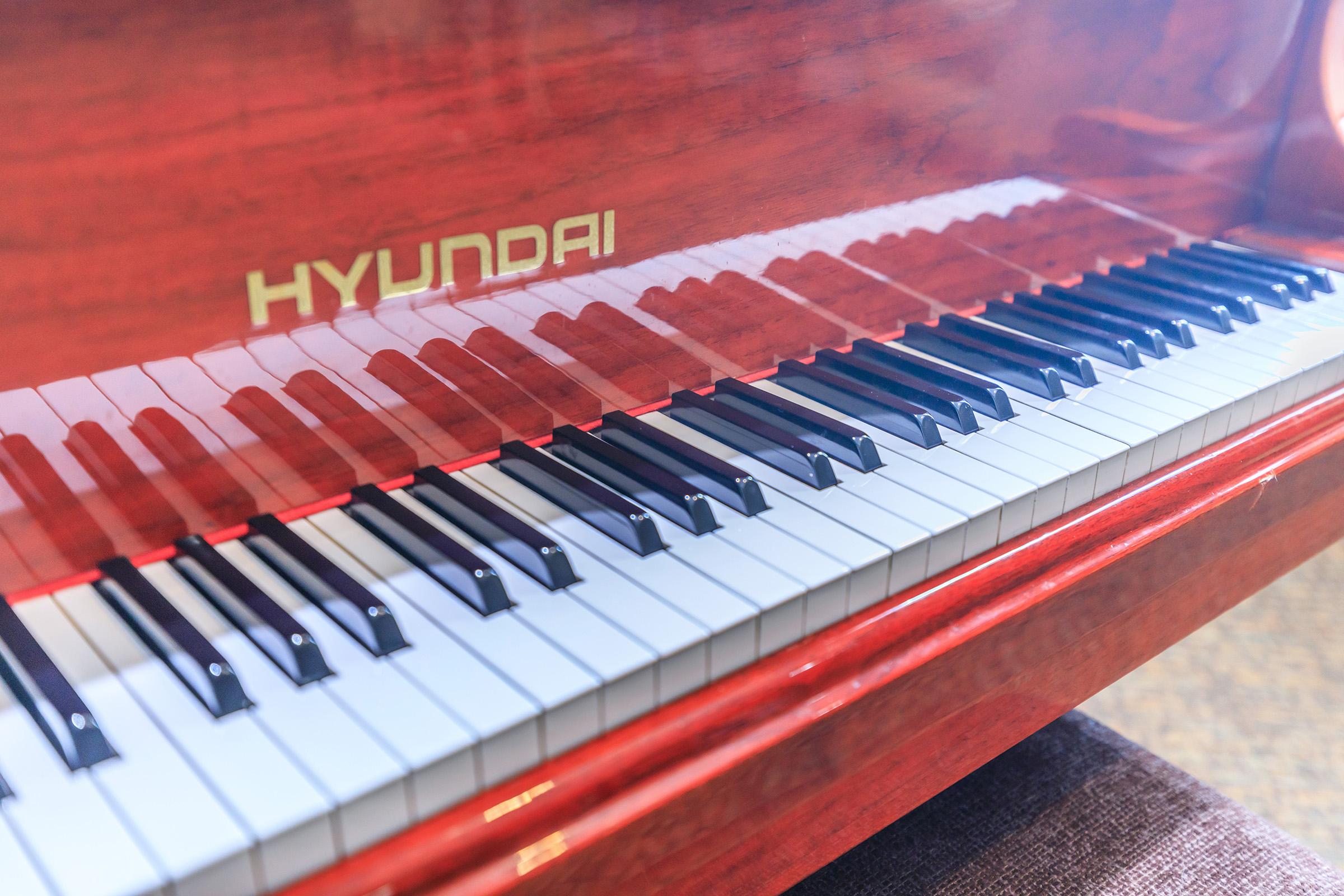 Close-up view of a Hyundai piano keyboard, featuring pristine white and black keys arranged in a traditional pattern, with a polished wooden finish reflecting light. The name "HYUNDAI" is prominently displayed on the piano's body. The image showcases the craftsmanship and design of the instrument.