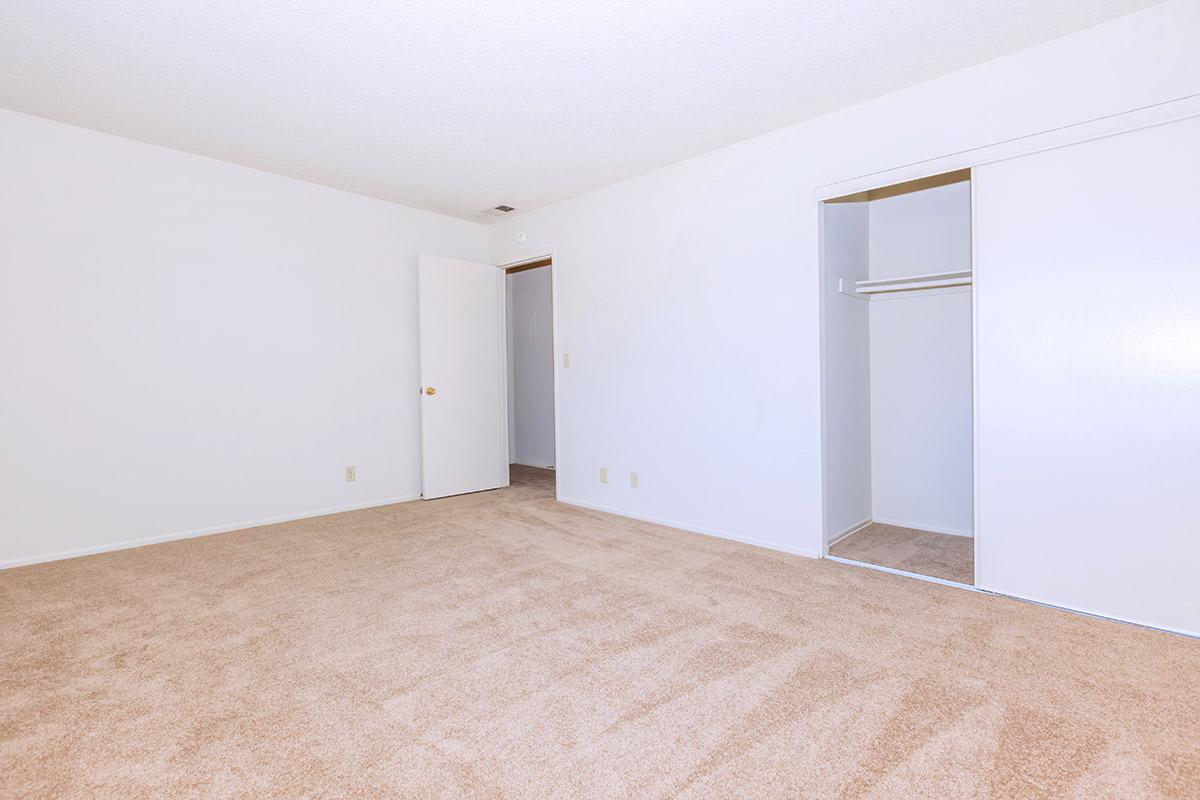 Empty room with white walls and a light beige carpet. A single door leads to another room, and there is a closet with sliding doors on the right side. The overall atmosphere is bright and spacious, emphasizing simplicity and minimalism.