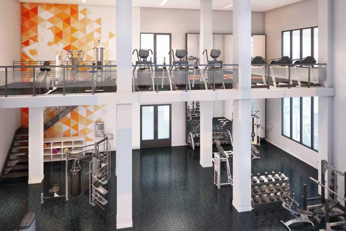 A modern gym interior featuring exercise machines on an upper level, with various workout equipment on the ground floor. The space is bright, with large windows and an orange geometric accent wall, showcasing a clean and inviting environment for fitness activities.