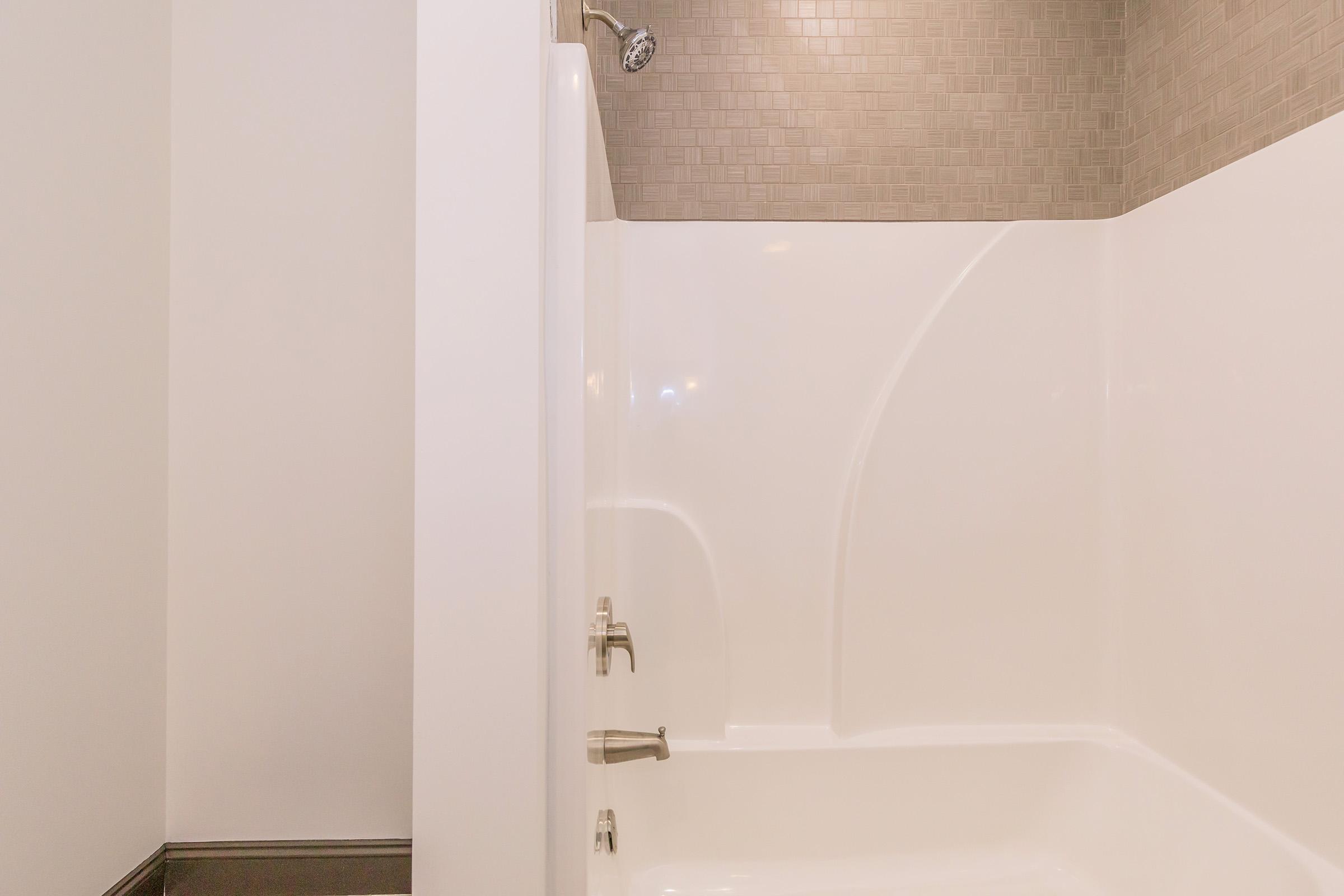 A clean, modern shower space with white walls and a textured gray tile accent. The shower features a curved wall, chrome fixtures, and a sleek design, creating a bright and inviting atmosphere.