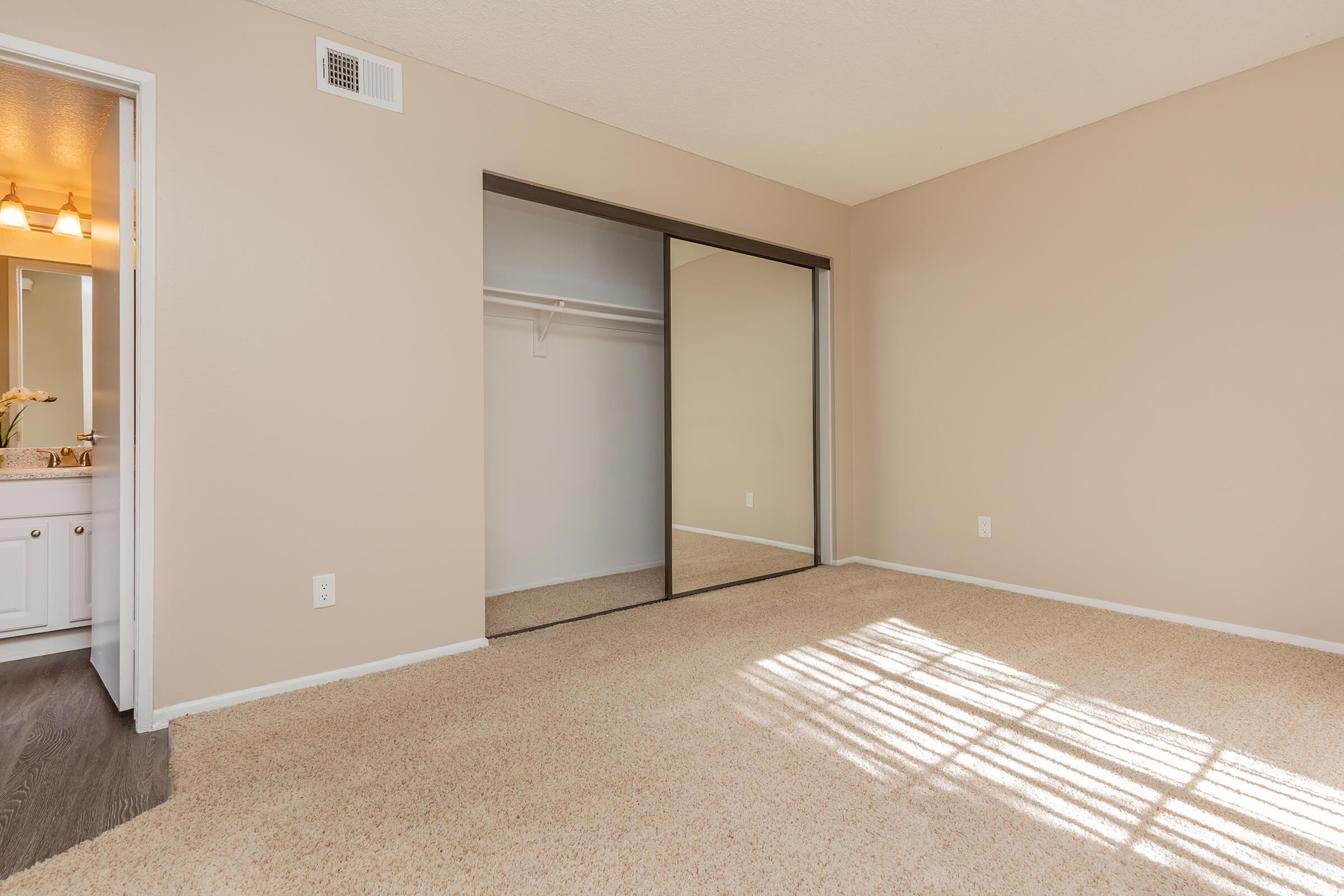 Carpeted bedroom with open sliding mirror glass closet doors