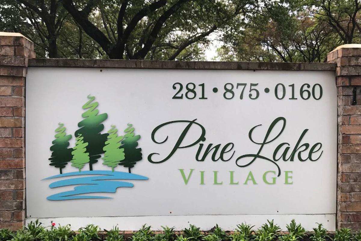 Sign for Pine Lake Village featuring stylized trees and water. The text includes the name "Pine Lake Village" prominently displayed, along with a phone number (281-875-0160). The background has a muted design with green and blue elements representing nature.