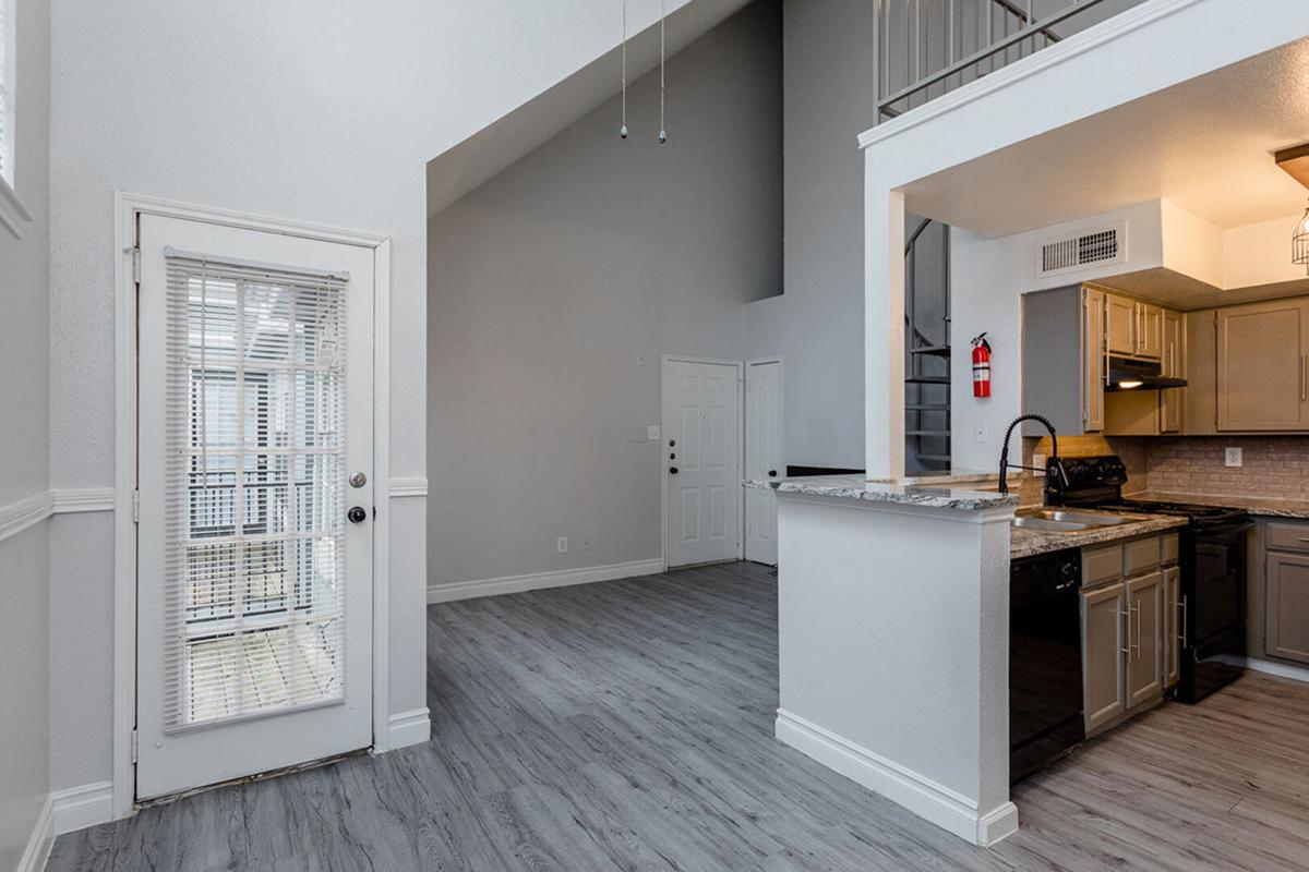 An inviting interior space featuring a modern kitchen with granite countertops, a cozy entrance with a door leading outside, and high ceilings. The room has light gray walls and sleek flooring, creating a bright and open atmosphere. Double doors lead to another room, enhancing the feeling of spaciousness.