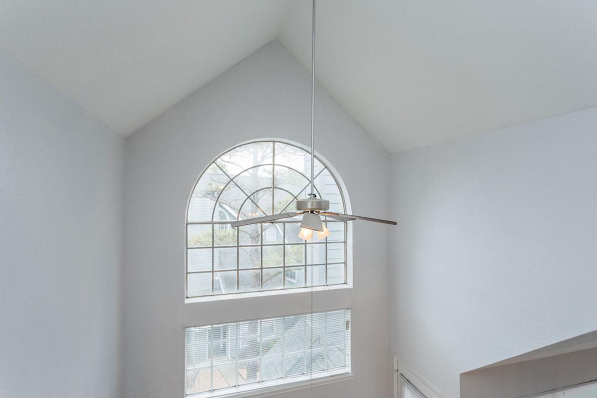 A well-lit room featuring a large arched window with a ceiling fan hanging from a high ceiling. The walls are painted in a light color, and there are blinds on the lower window, enhancing the airy and spacious feel of the interior.