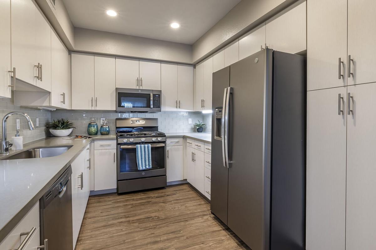 Modern kitchen featuring white cabinetry, stainless steel appliances, a gas stove, and a microwave. The countertop is light gray, and there are potted plants for a touch of greenery. The floor is wooden and the space is well-lit with recessed lighting.