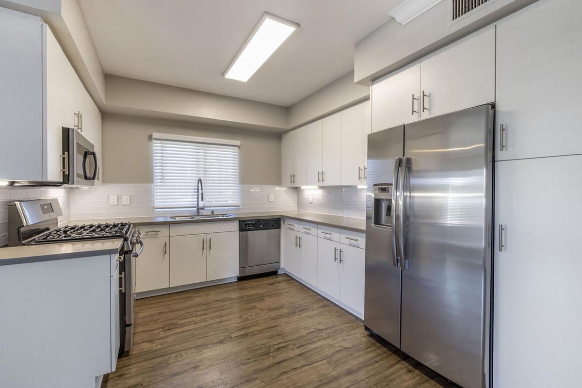 Modern kitchen featuring white cabinets, stainless steel appliances, and a gray wall. Includes a gas stove, microwave, and dishwasher, along with a window above the sink providing natural light. The floor is a wood-like laminate, creating a warm and inviting atmosphere.