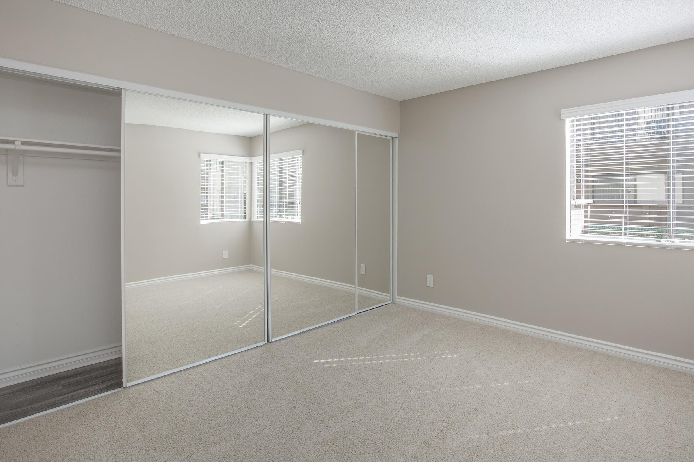 Carpeted bedroom with open sliding mirror glass closet doors
