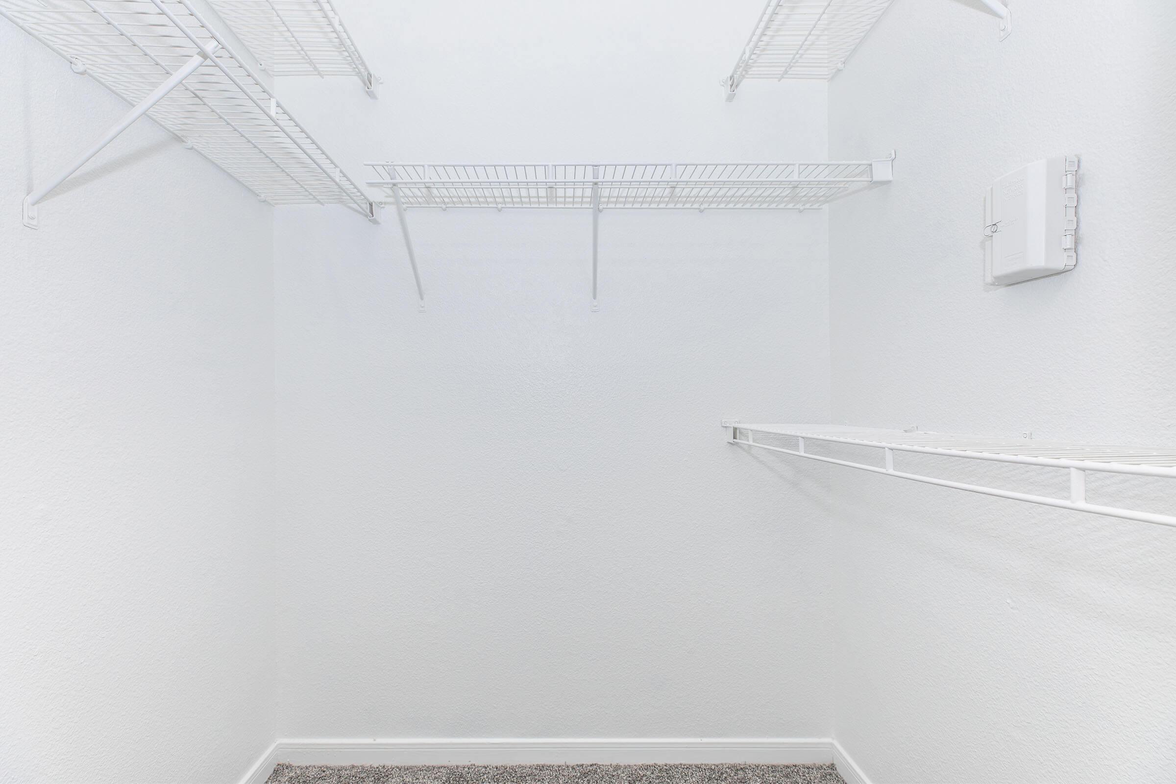 An empty closet with white wire shelving against plain white walls, featuring a carpeted floor. The space is uncluttered, highlighting the absence of items or decoration.