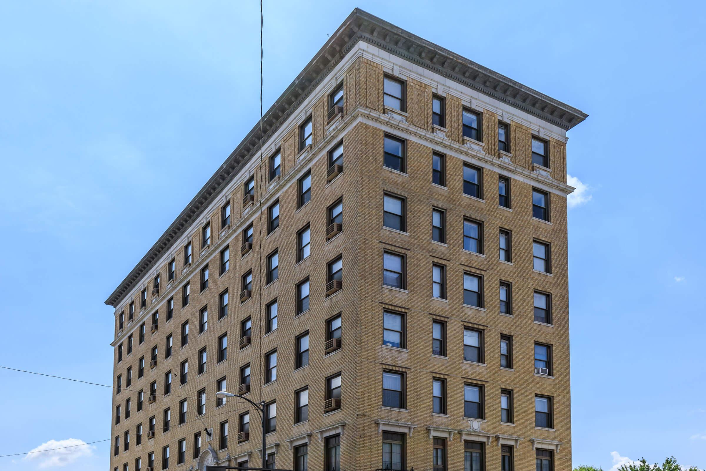 A tall, six-story brick building with large windows, set against a clear blue sky. The architectural style features classic elements, including a decorative cornice at the top and a vertically oriented design. The building appears well-maintained and is likely part of an urban landscape.