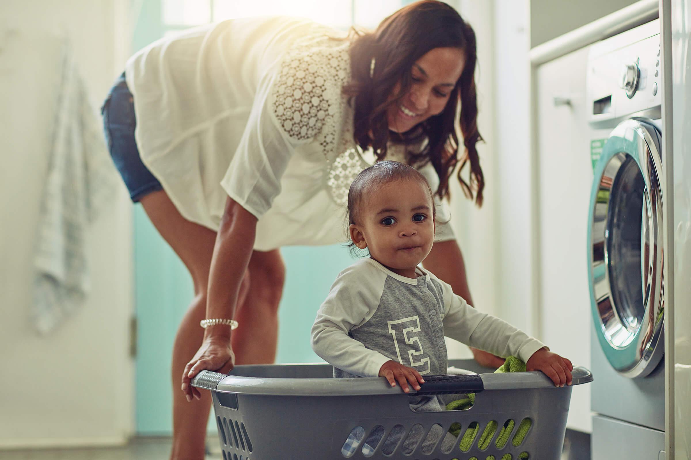 a woman pushing a laundry basket with a child inside