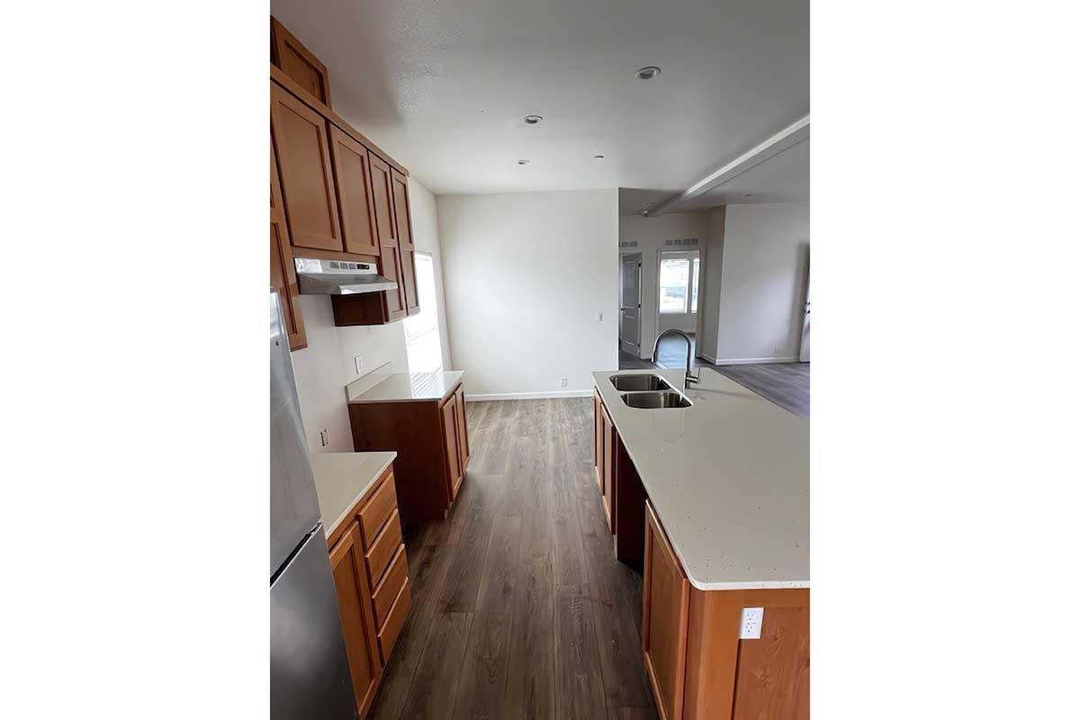 Modern kitchen featuring wooden cabinets, a central island with a sink, stainless steel appliances, and abundant natural light. The space has a neutral color palette with wood-look flooring, creating a bright and inviting atmosphere. Suitable for cooking and entertaining.