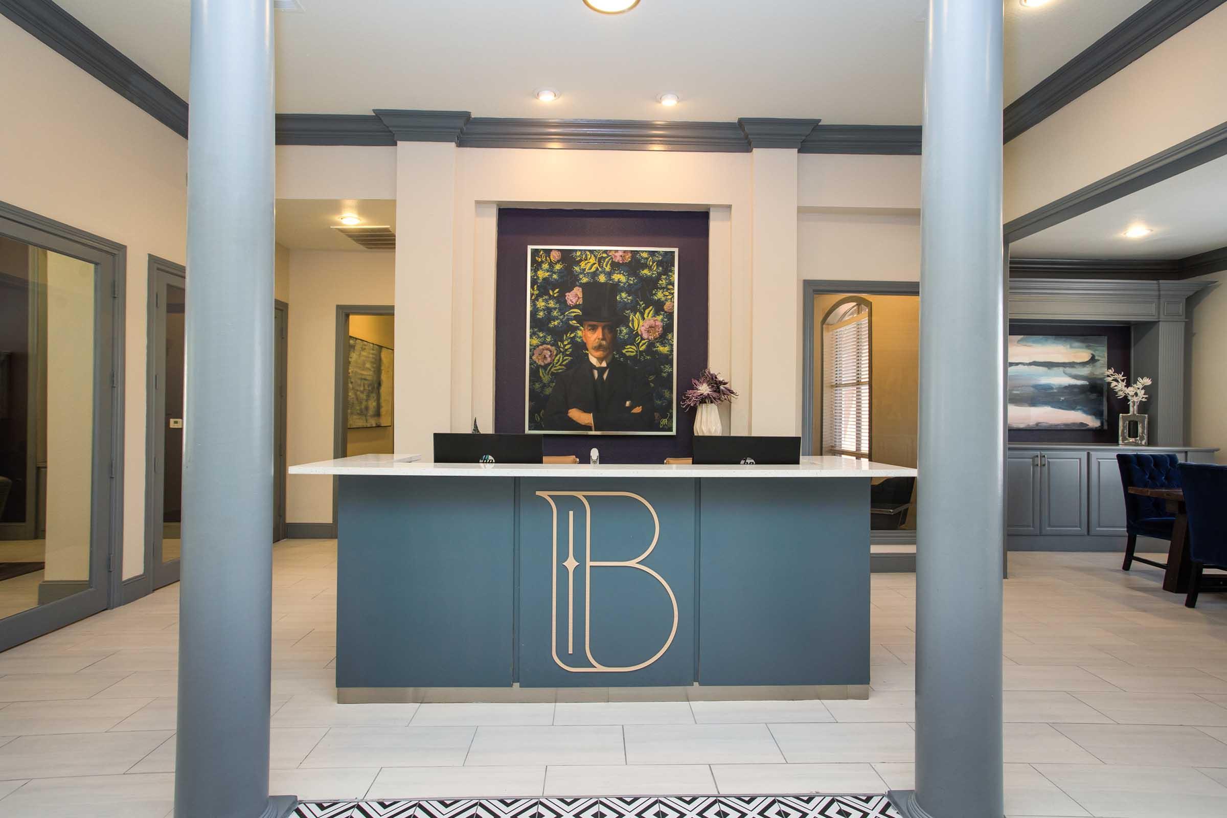 Modern reception area featuring a stylish front desk with a sleek design and a prominent floral artwork on the wall. The space includes grey and white tones, large columns, and decorative touches, creating a welcoming atmosphere in a professional setting.