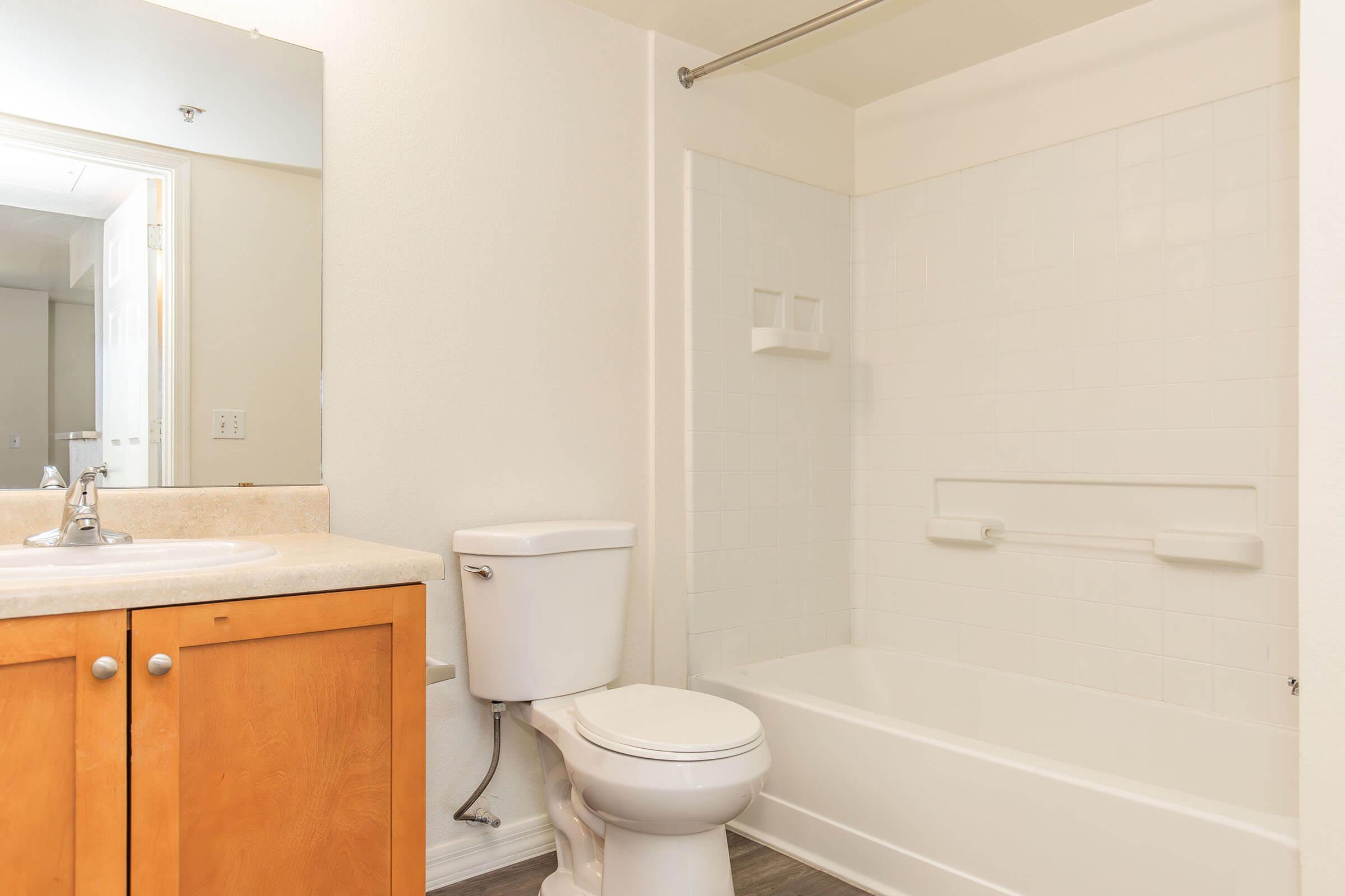 A clean and modern bathroom featuring a white shower and bathtub, a toilet, and a wooden vanity with a sink. The walls are painted in light colors, enhancing the spacious feel, and there is good lighting from an unseen source. The space appears well-maintained and inviting.