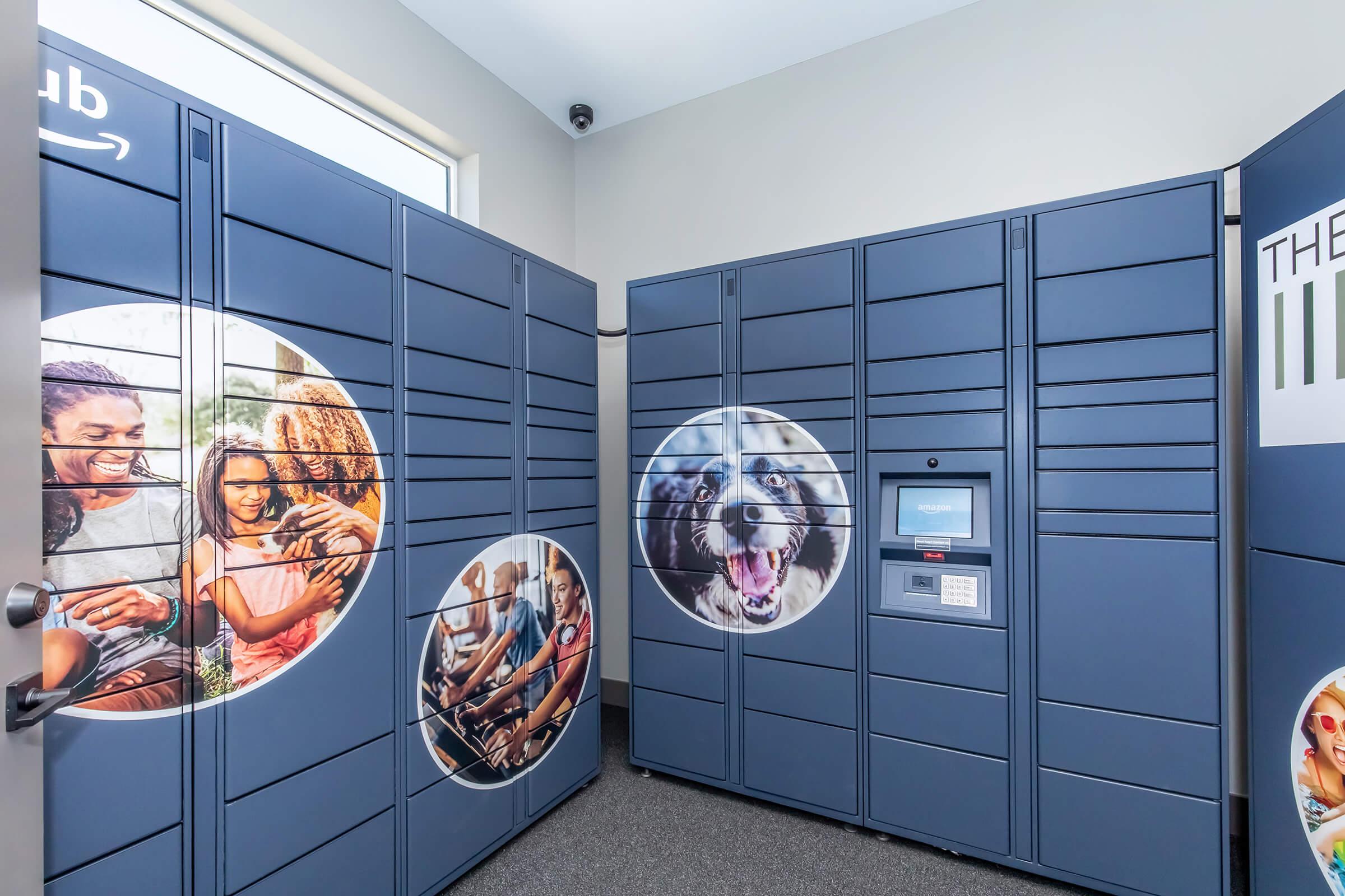 A modern Amazon Locker area featuring multiple blue lockers. The lockers have rounded images on the sides showing diverse individuals enjoying various activities and a playful dog. There is an access panel on the front of the lockers for users to retrieve their packages. The setting is bright and inviting.