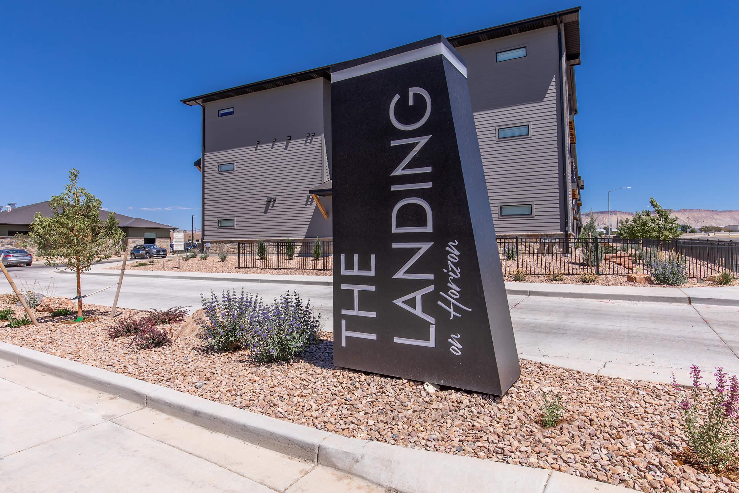 Sign for "The Landing on Horizon" near a residential building, with modern architecture in the background. The area features landscaping with rocks, small plants, and a clear blue sky.