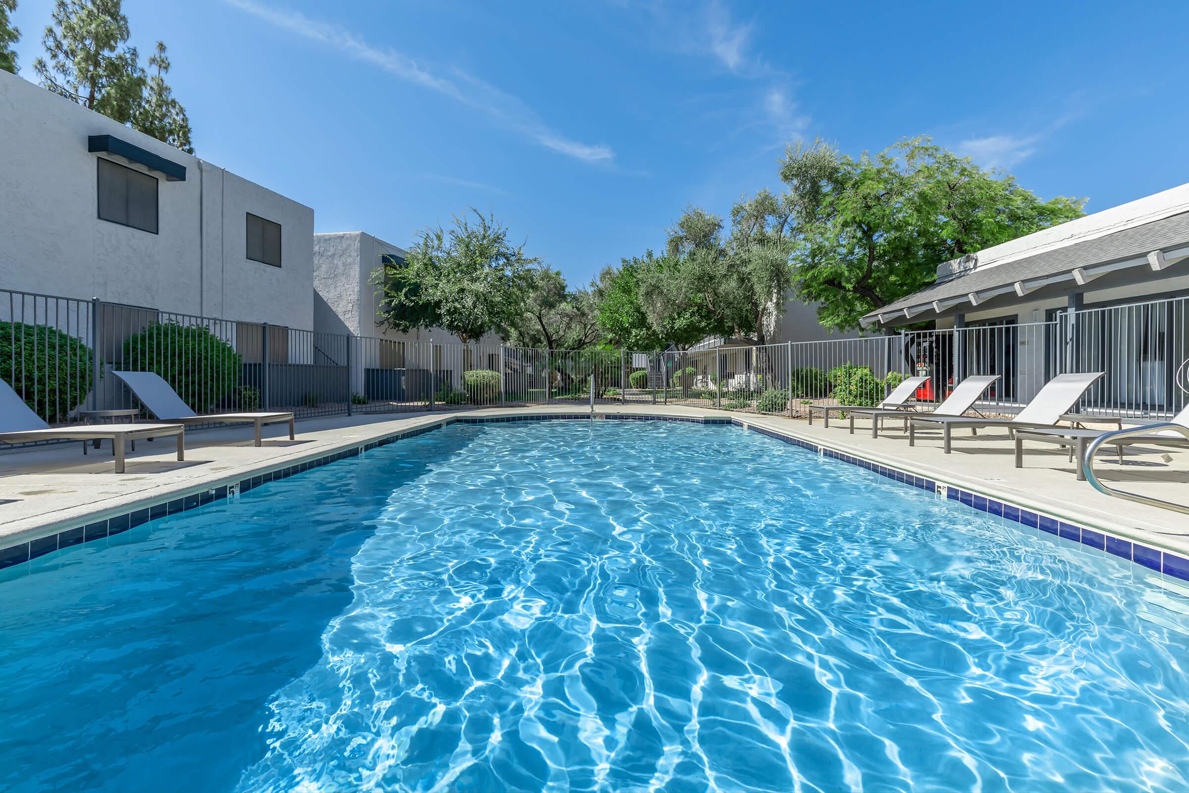 Large blue sparkling resort style pool surrounded by pool deck chairs