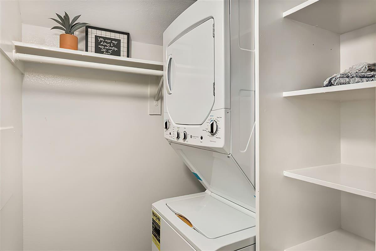Stacked washer and drier next to shelves and storage space