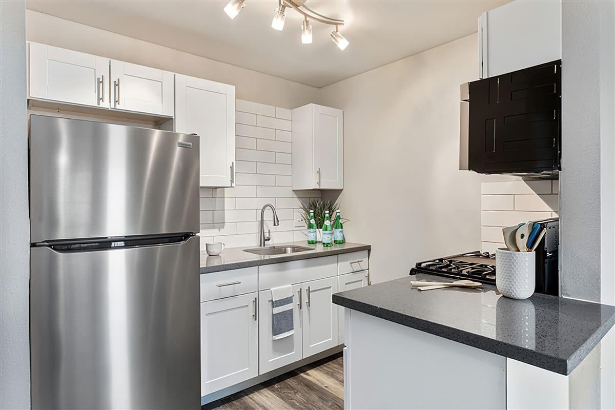 Renovated kitchen with a stainless steel fridge, white shaker cabinets, and grey quartz countertops