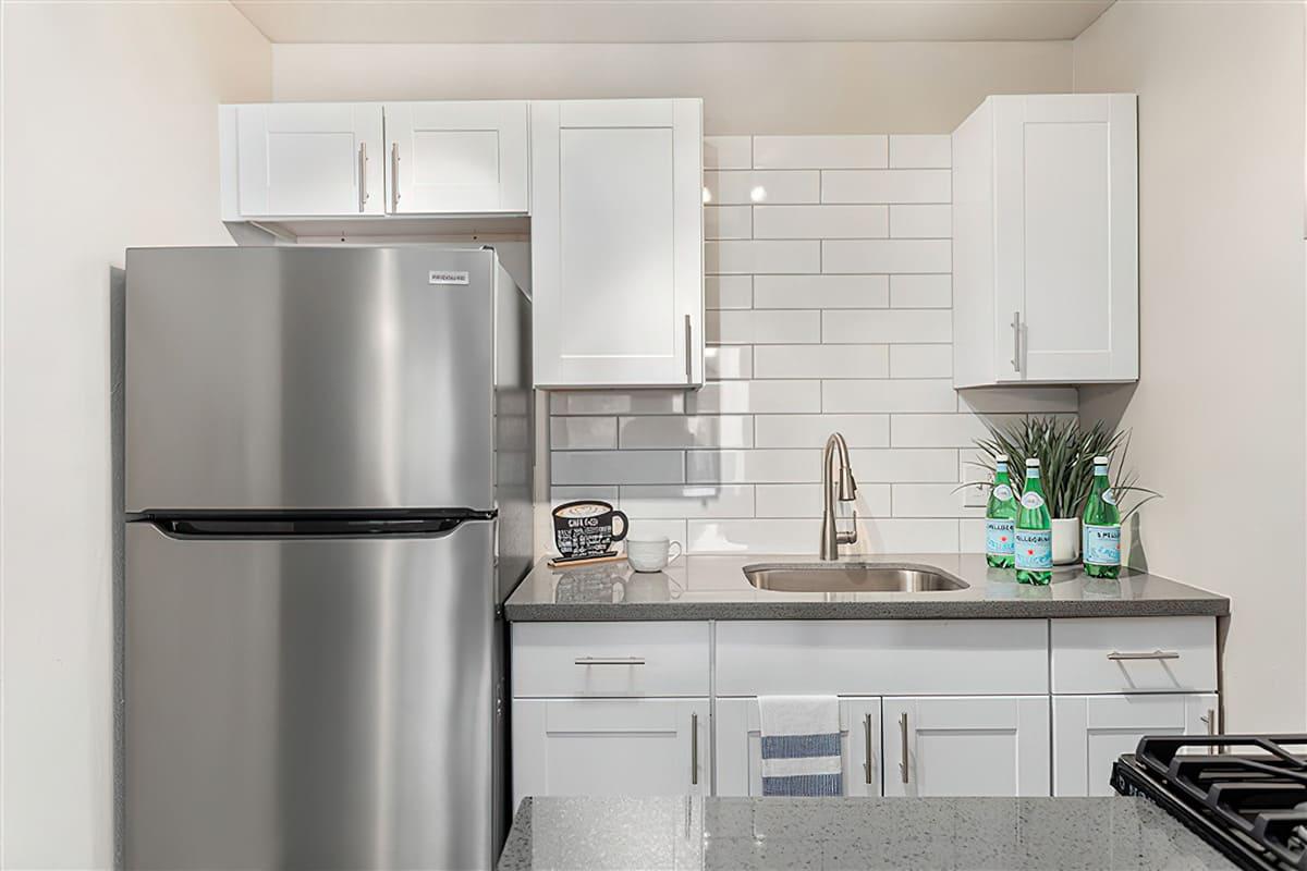 Renovated kitchen with a stainless steel fridge, white shaker cabinets, and grey quartz countertops