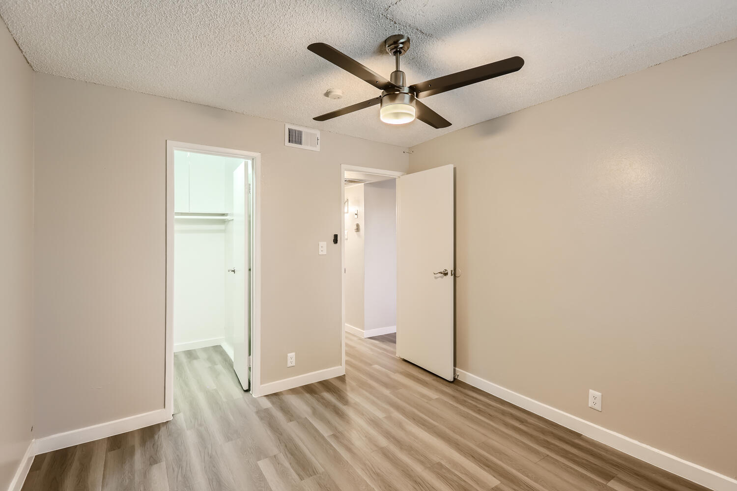 A small bedroom with wood-style flooring and a walk-in closet at Rise at the Preserve.