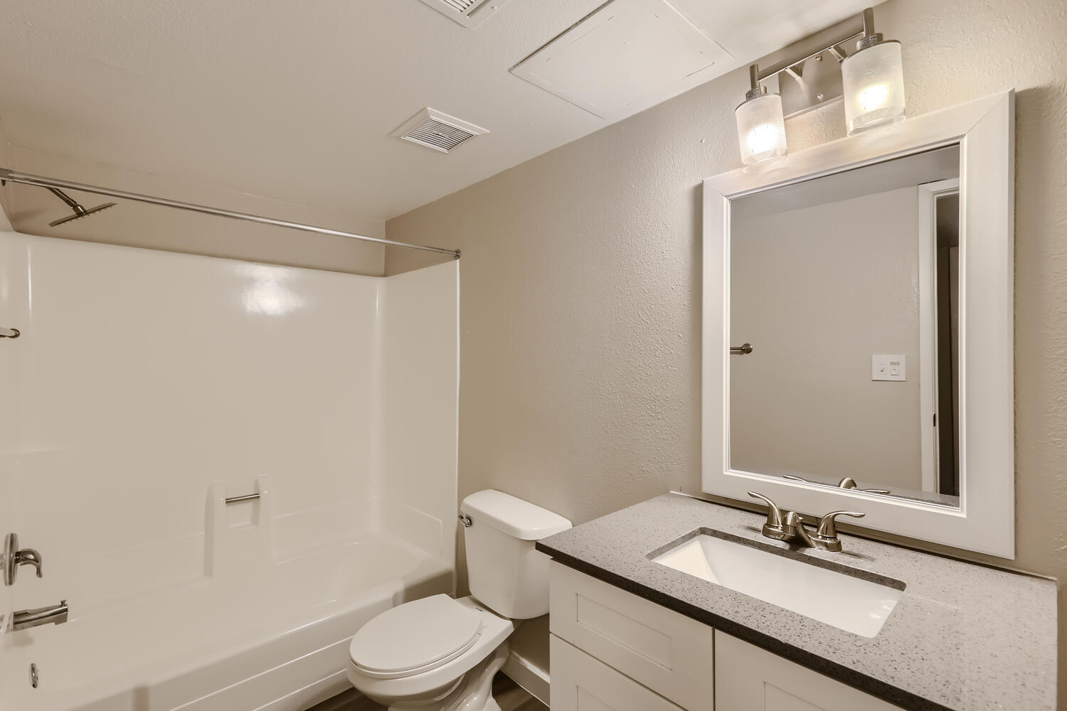 A remodeled bathroom with grey quartz countertops and a tub at Rise at the Preserve.