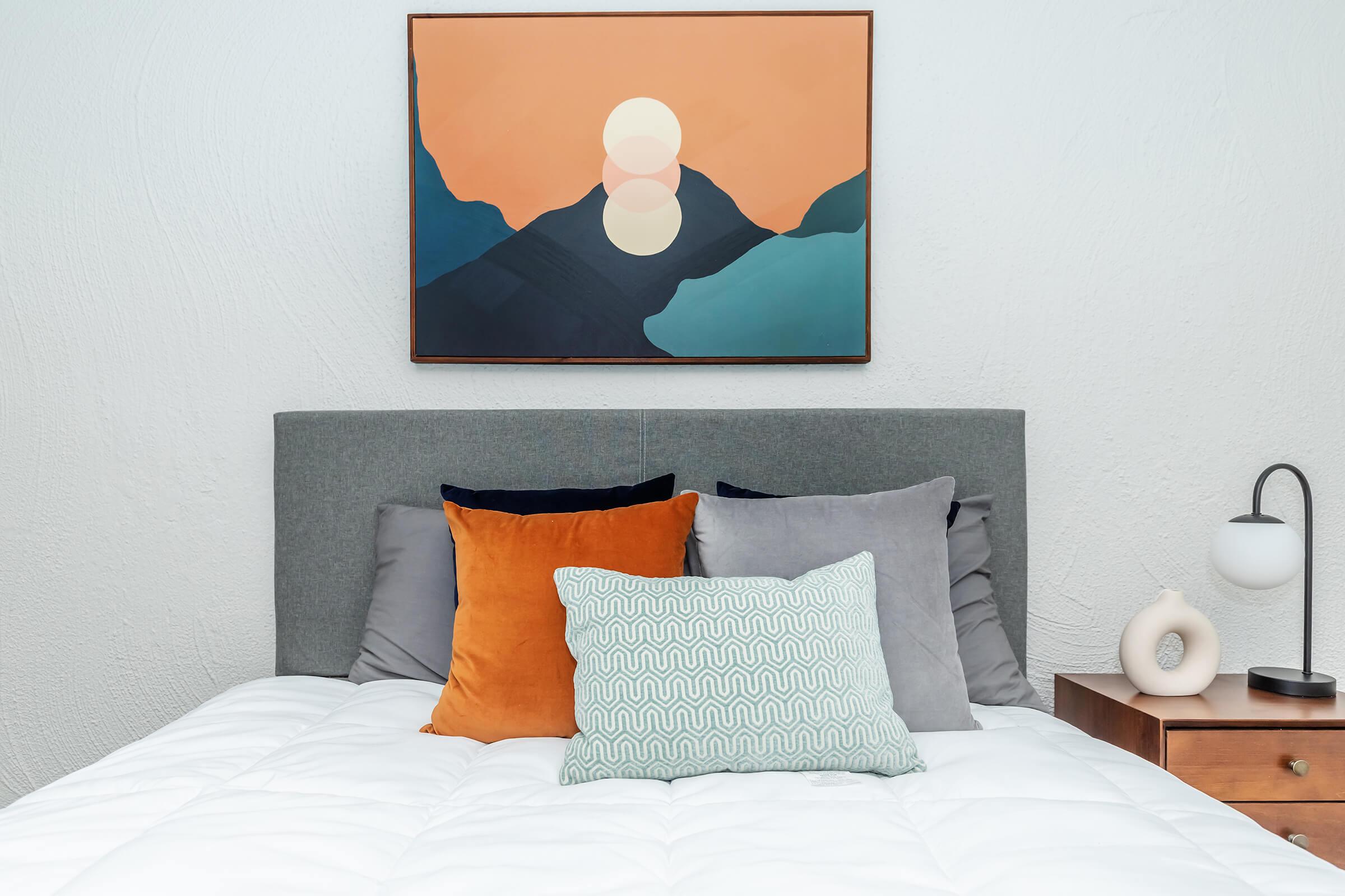 A bed with colorful pillows and a painting above it at Rise at the Preserve. 