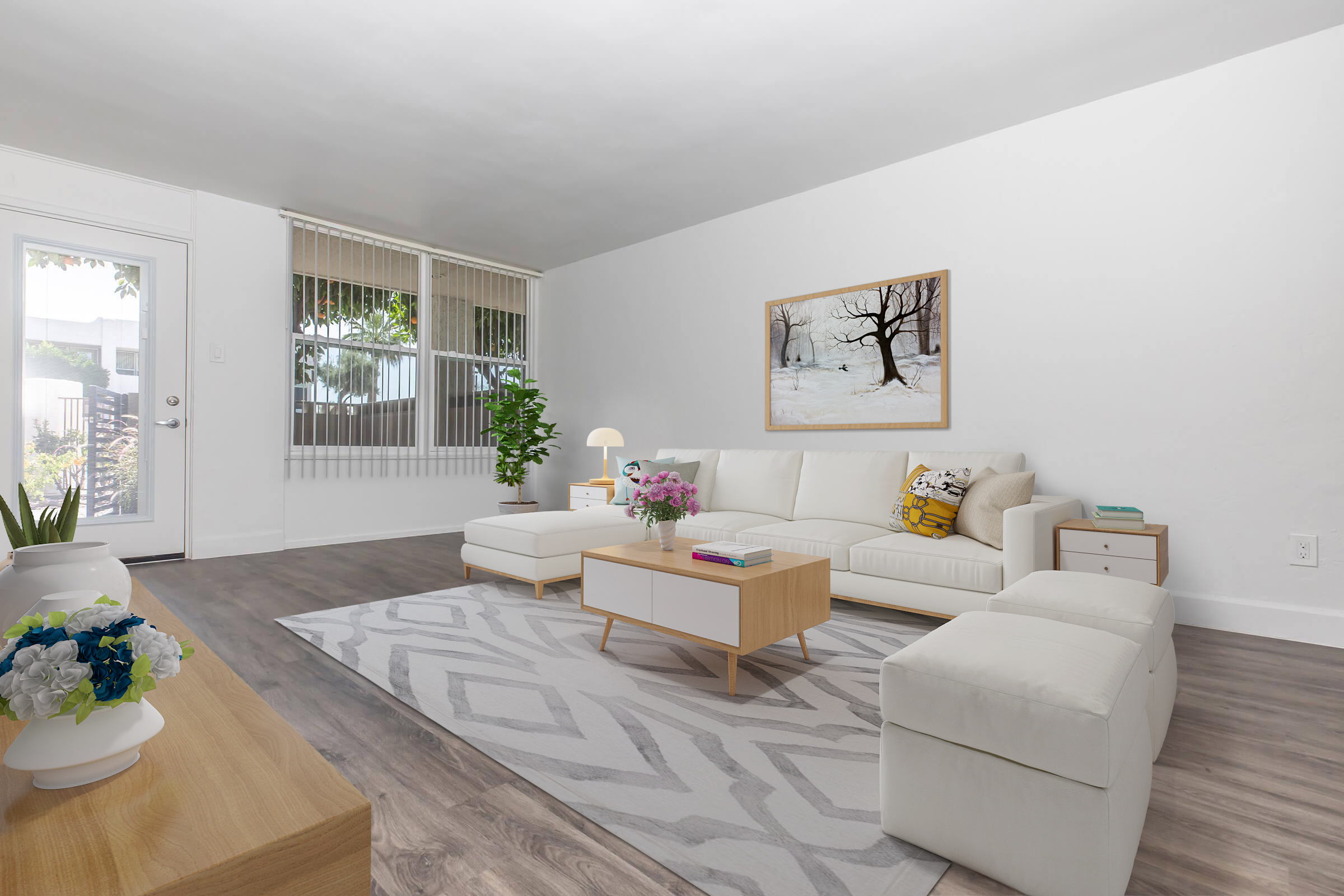 Bright and airy living room featuring a white sectional sofa, a light wooden coffee table, and decorative pillows. A large framed artwork of a winter scene hangs on the wall. The room has light-colored walls, a potted plant near the door, and a patterned area rug on the floor, creating a cozy and inviting atmosphere.