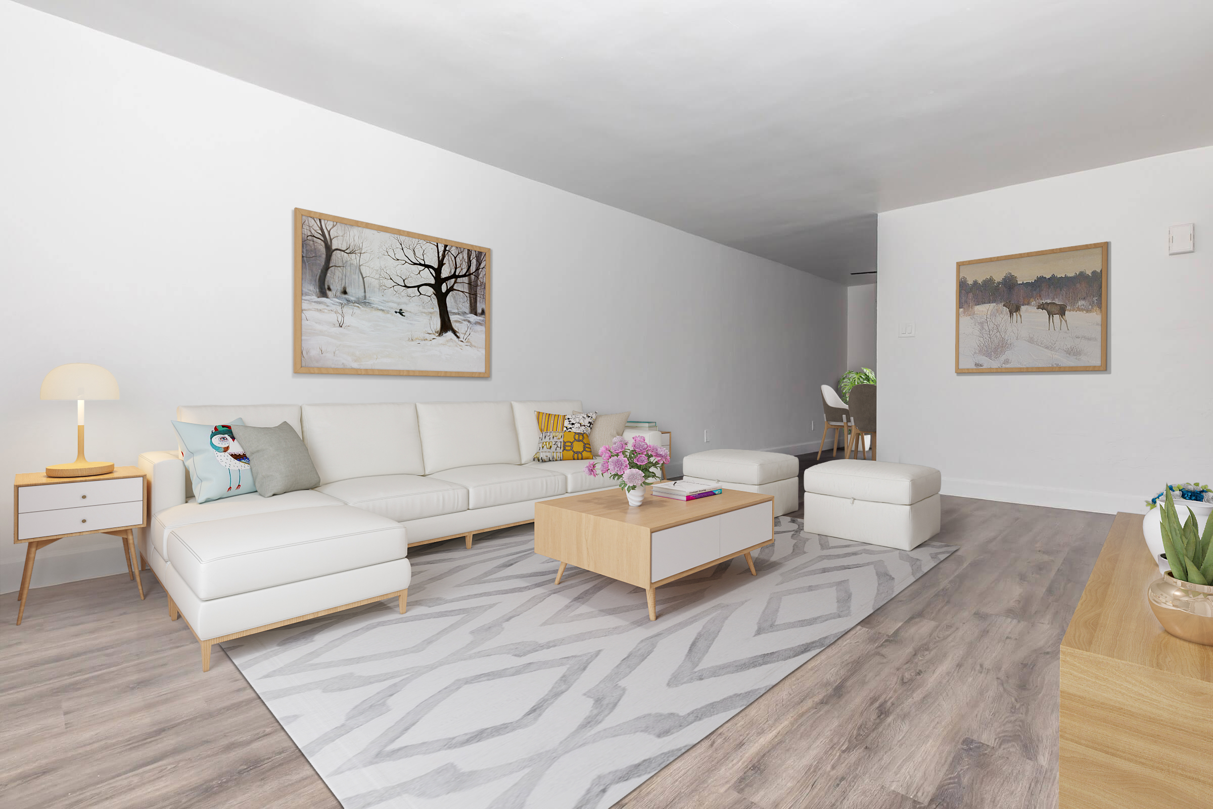 A modern, minimalist living room featuring a light-colored sectional sofa, a wooden coffee table, and a cozy area rug with a geometric pattern. Two framed paintings hang on the walls, and a small lamp and decorative plants add warmth to the space. The room has a bright, airy feel with natural light.