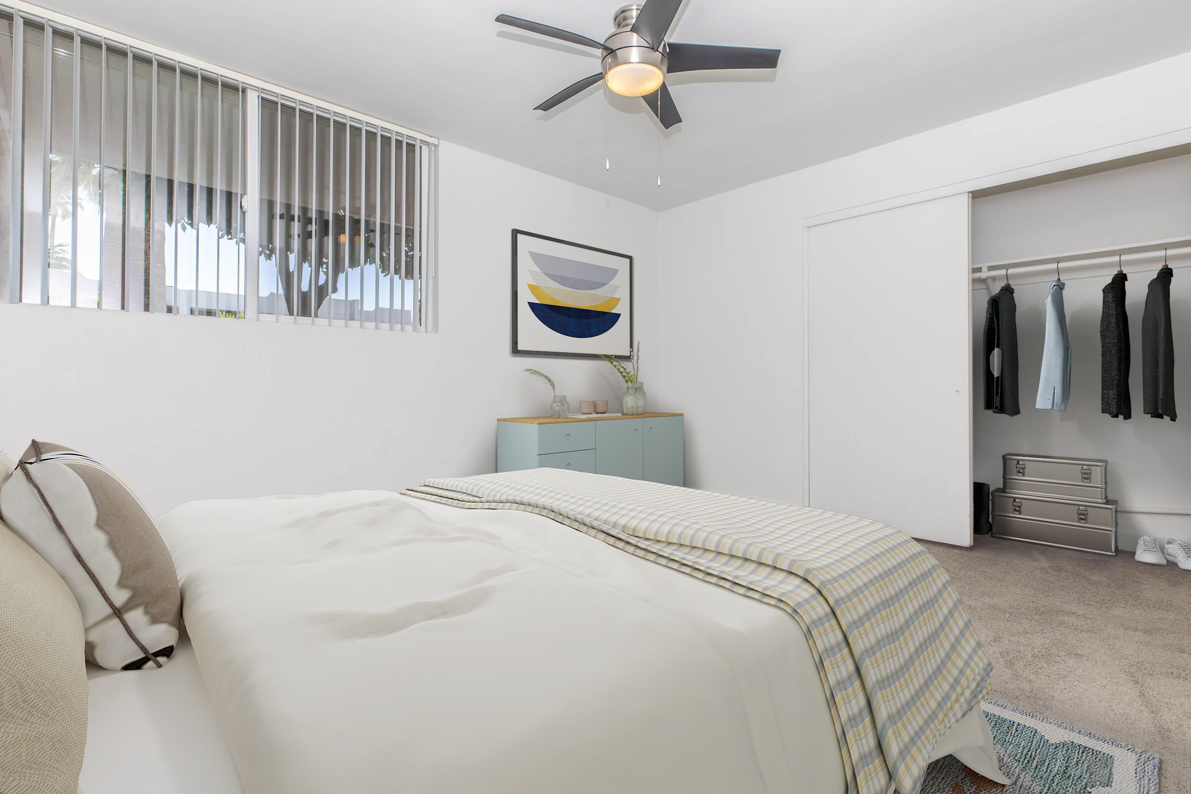 A modern bedroom featuring a queen-sized bed with neutral bedding, a ceiling fan, and a minimalist design. There is a closet with hanging clothes and a light blue dresser against the wall. Large windows allow natural light to fill the room, and a framed abstract artwork is displayed above the dresser.