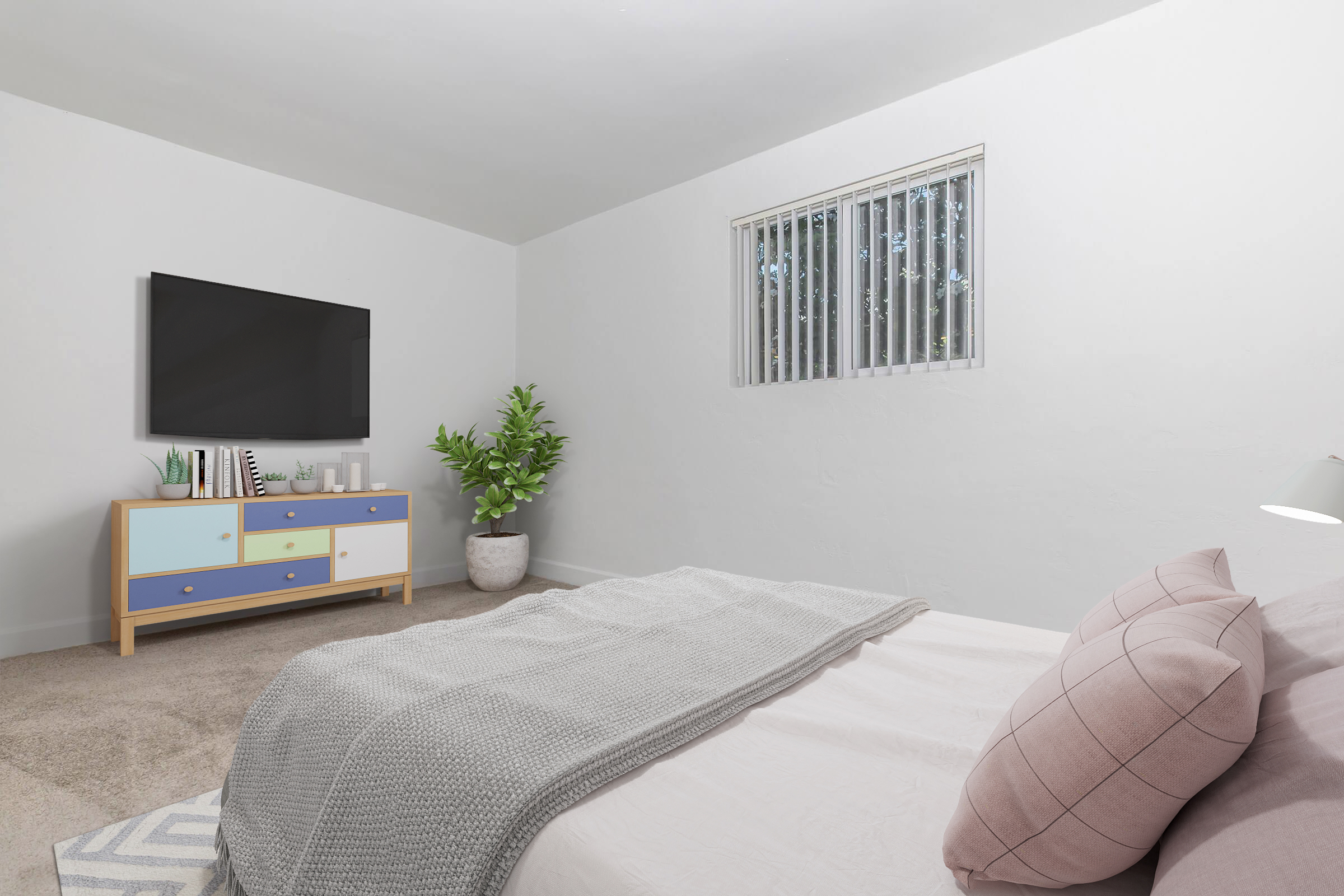 A cozy bedroom featuring a neatly made bed with light gray bedding and two pink pillows. A flat-screen TV mounted on the wall is above a light wood dresser with colorful drawers. A potted plant adds a touch of green, and a window with blinds allows natural light to enter the room. Soft carpet covers the floor.