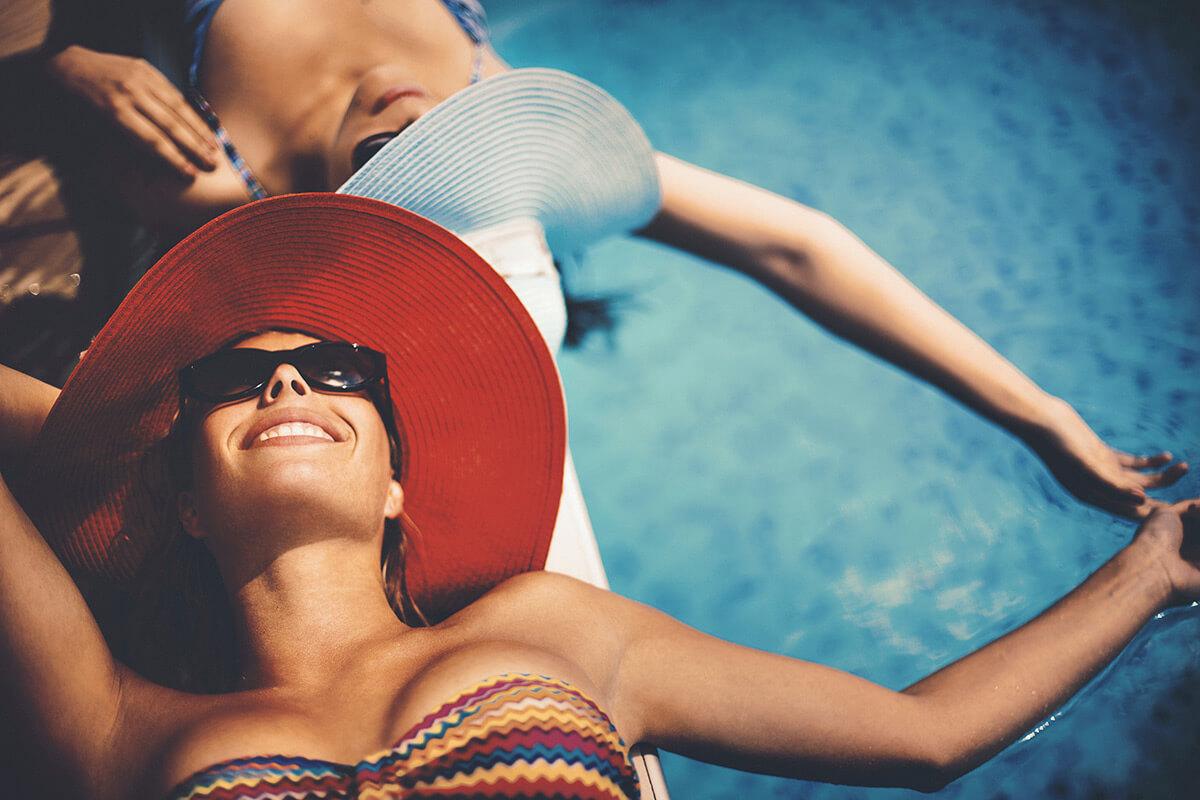 Two women by the pool with sunhats