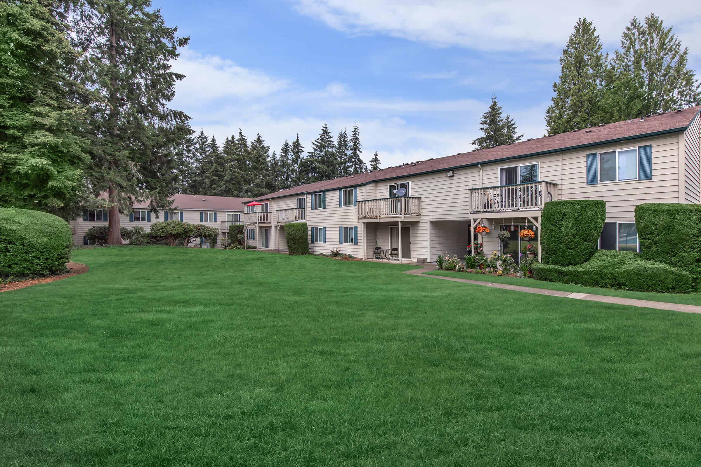 a large lawn in front of a house with Lake Quinault Lodge in the background