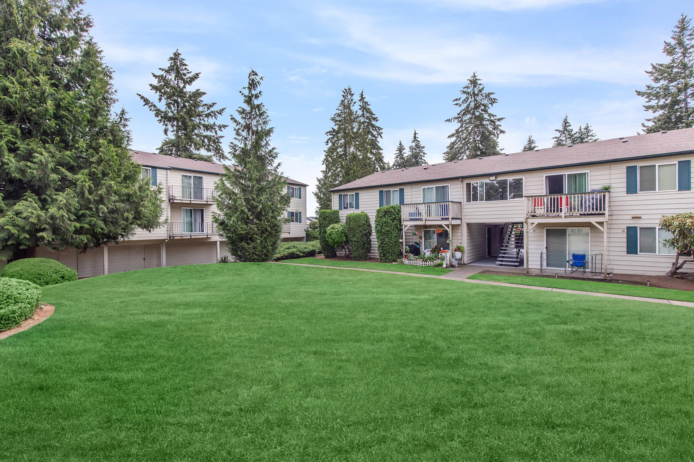 a large lawn in front of a house with Lake Quinault Lodge in the background